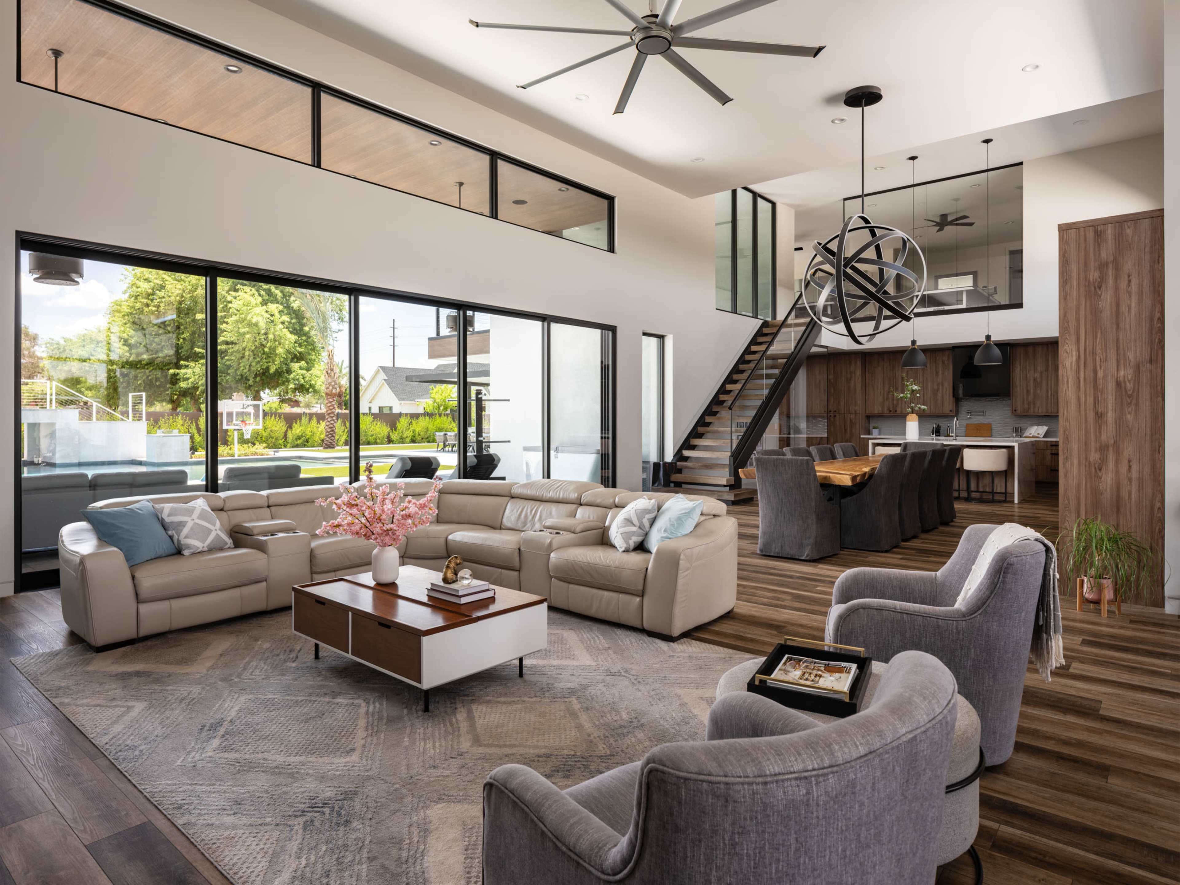 The image features a modern living room with a sectional sofa, a coffee table, and large windows that overlook a patio area.