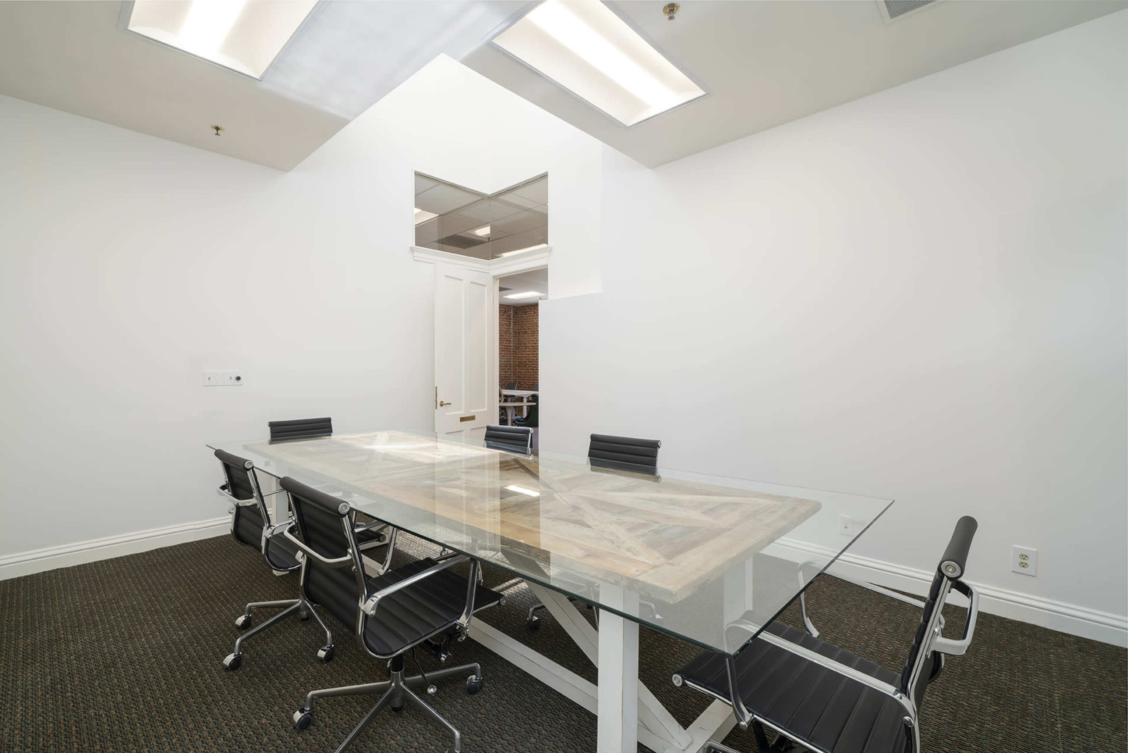 A modern conference room with a glass table surrounded by black office chairs and a door leading to another space.