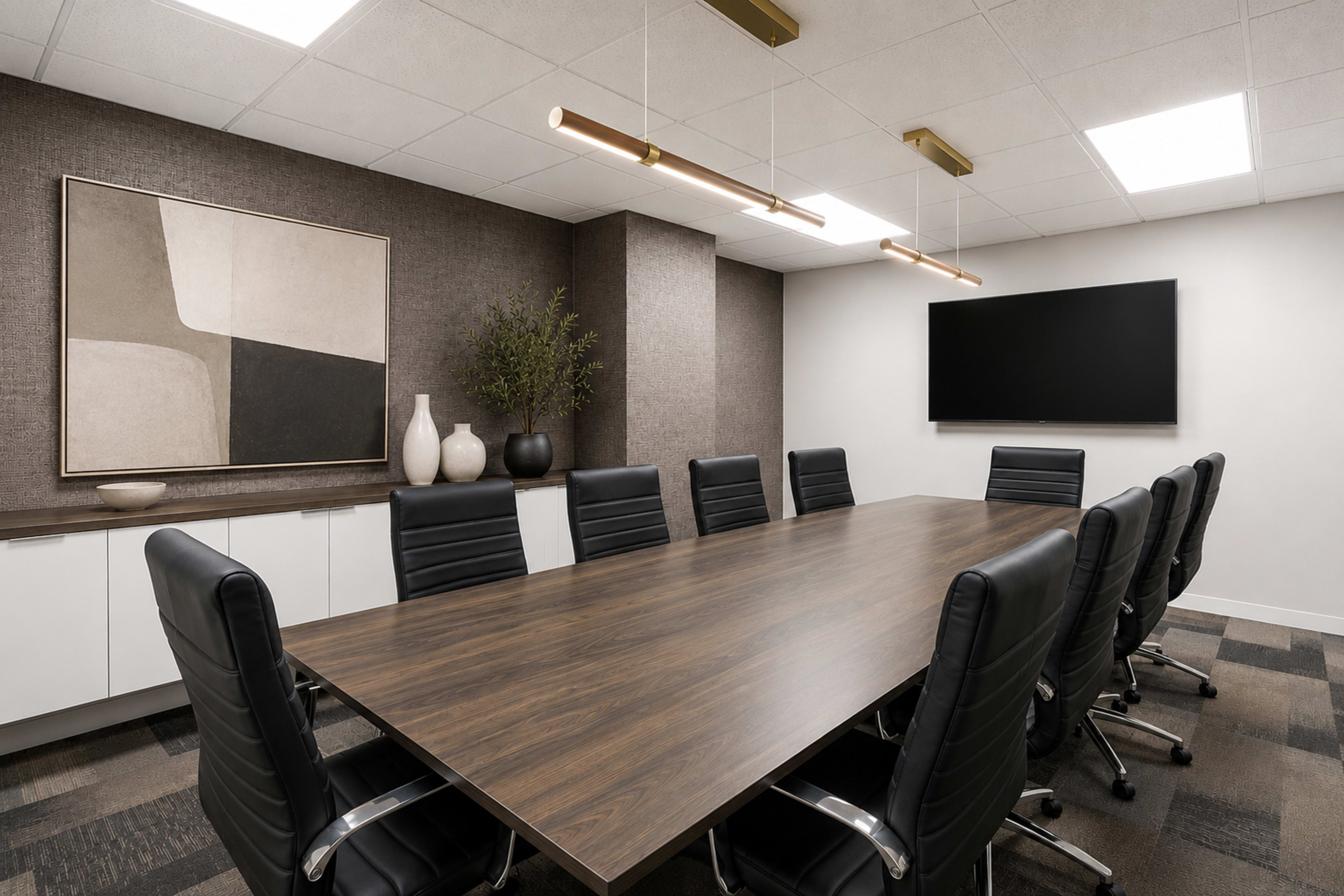 A modern conference room features a large wooden table surrounded by black leather chairs, with abstract wall art and a flat-screen television mounted on the wall.