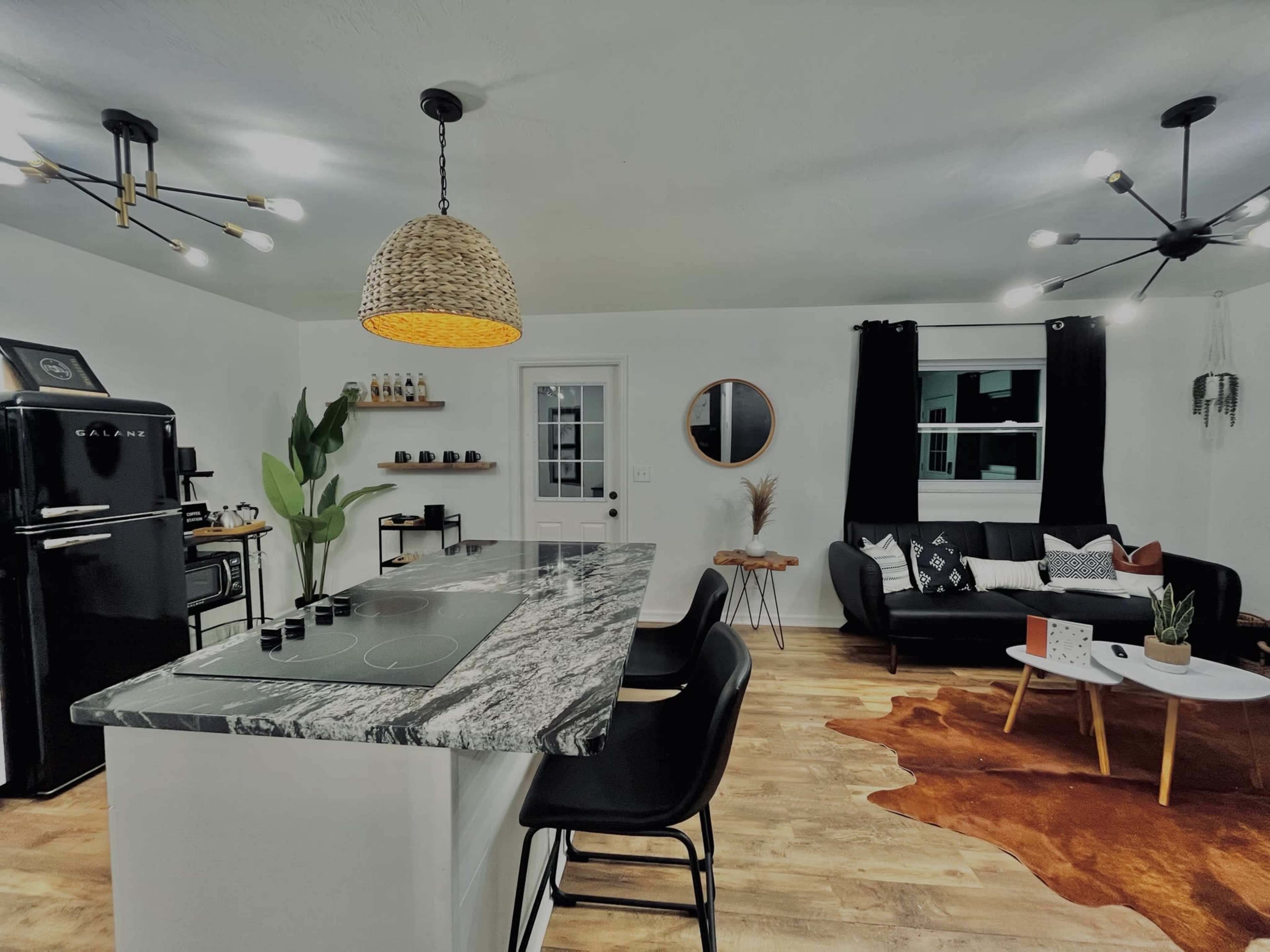 A modern kitchen and living area feature a marble countertop island, black chairs, a retro fridge, and a combination of dark and light decor.