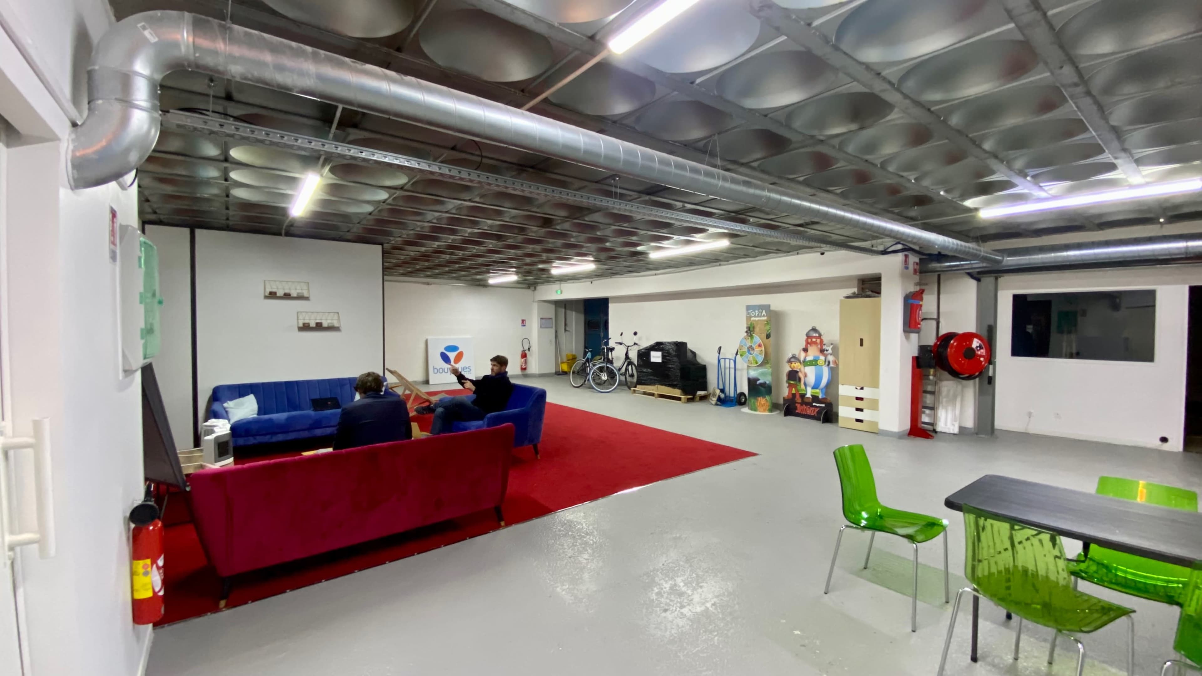 A spacious indoor area with colorful couches, a red carpet, bicycles, and a table surrounded by green chairs.