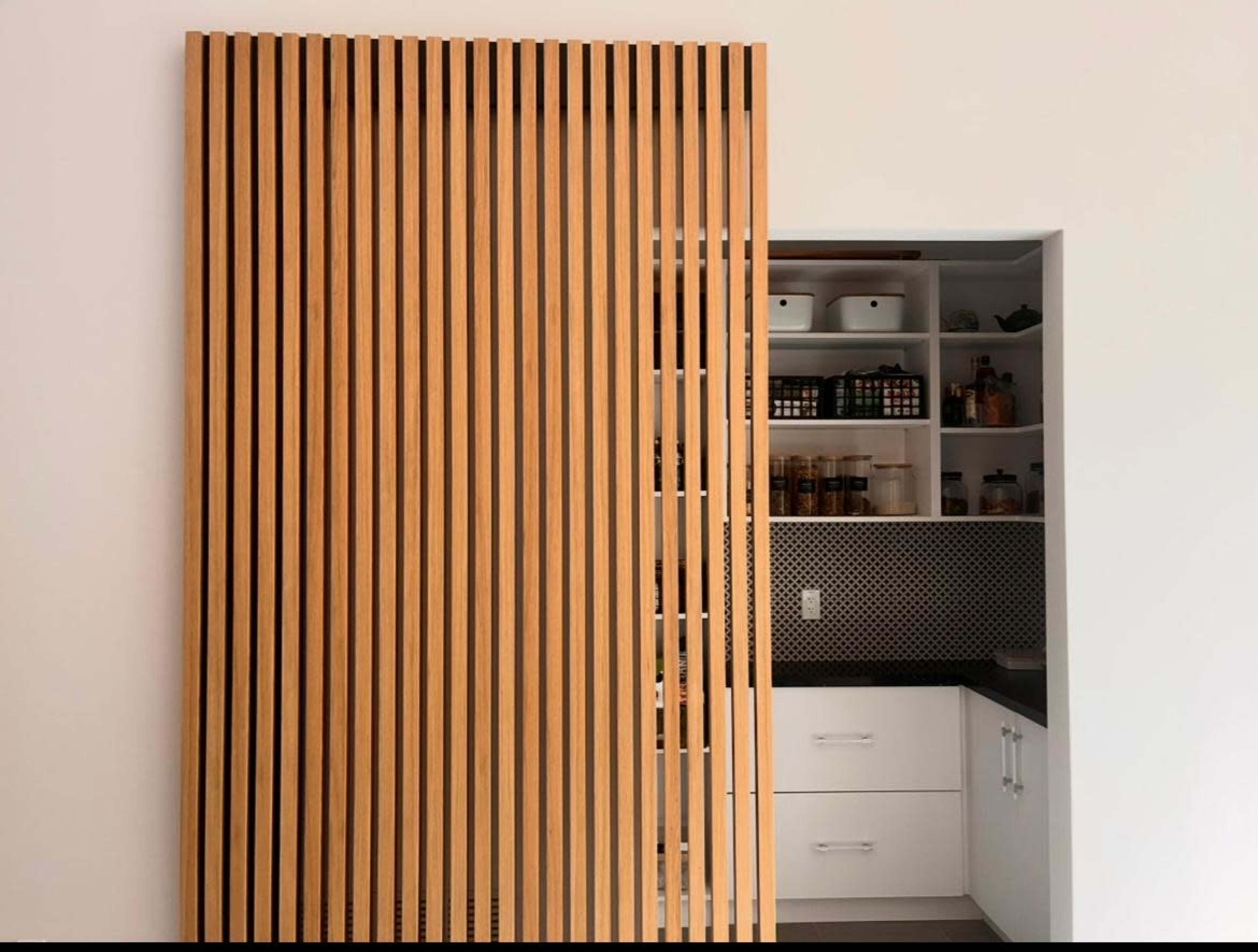 The image shows a wooden slatted door leading to a small pantry with shelves filled with jars and containers.