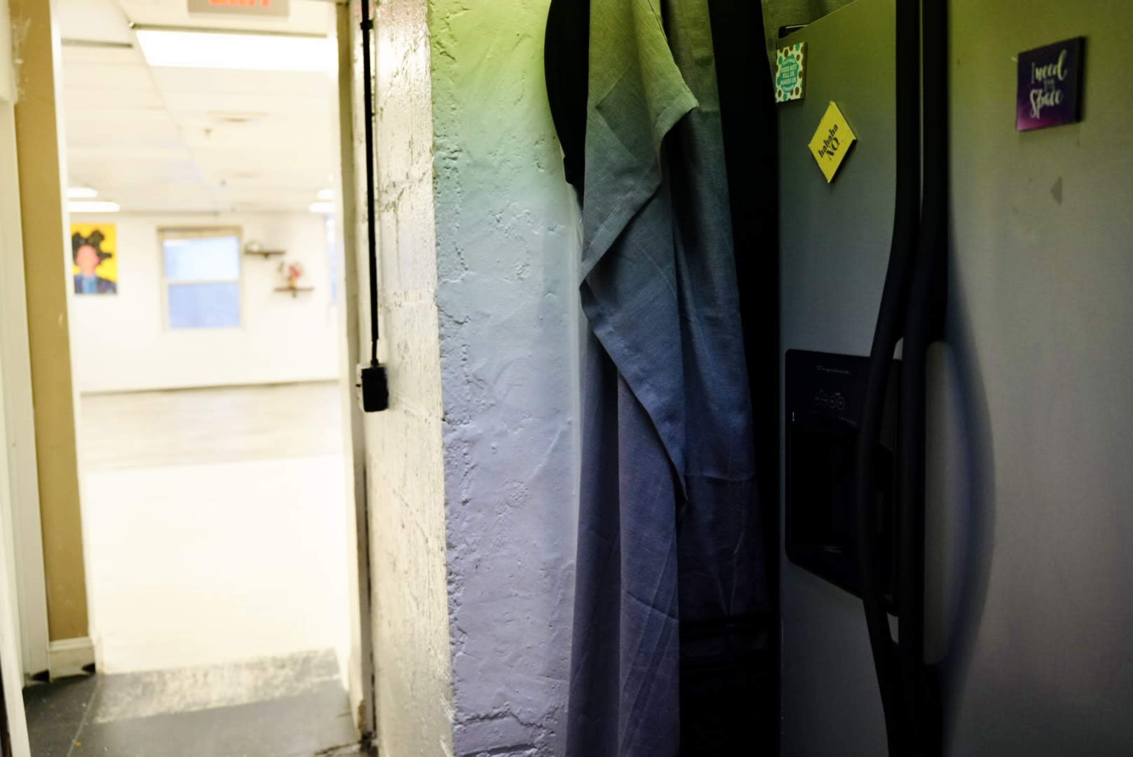 A gray curtain hangs next to a refrigerator in a partially visible room with a plain floor and a white wall.