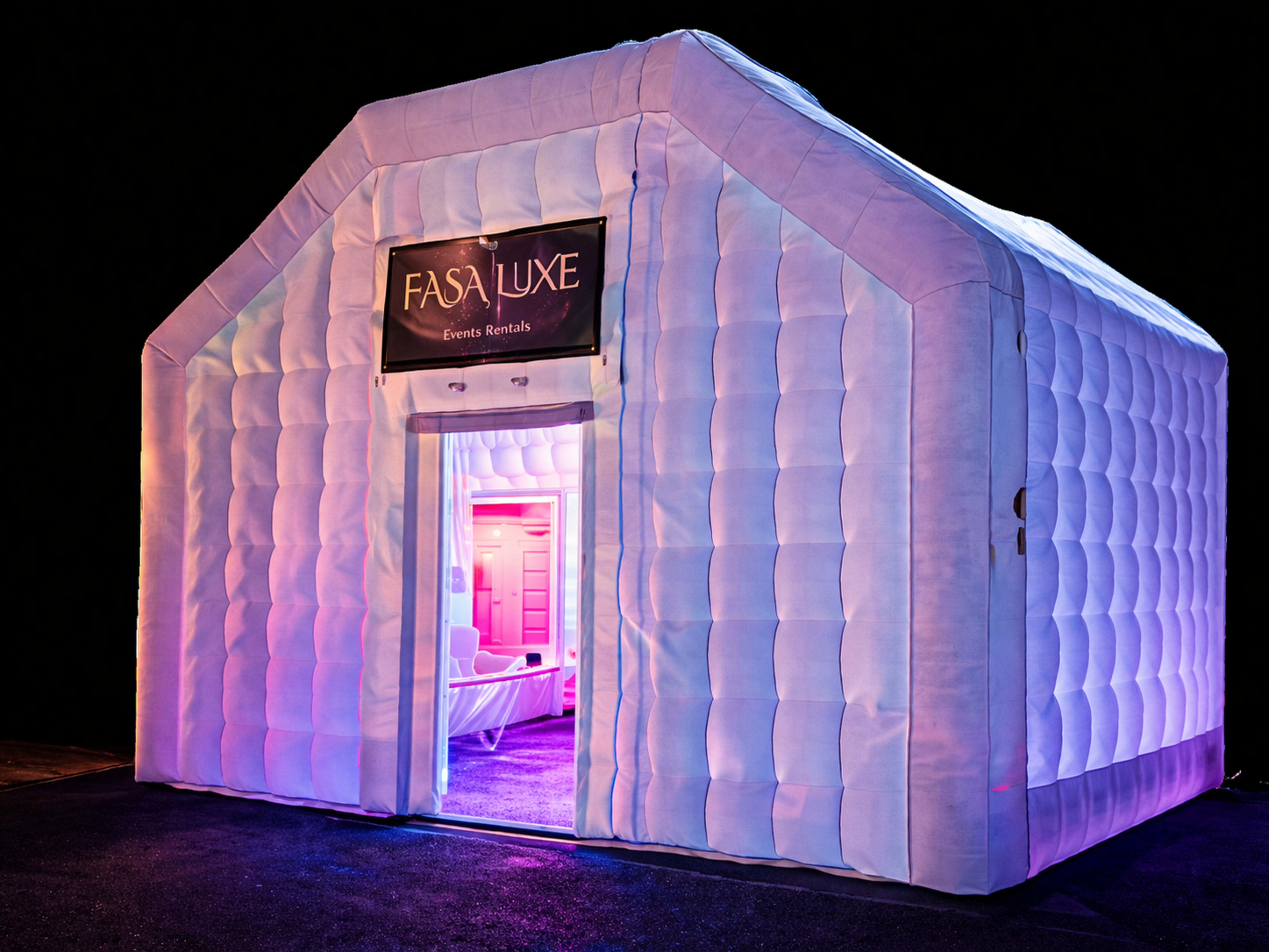 A large, inflatable white structure with a pitched roof and a brightly lit entrance displays a sign that reads "Fasa Luxe Events Rentals."