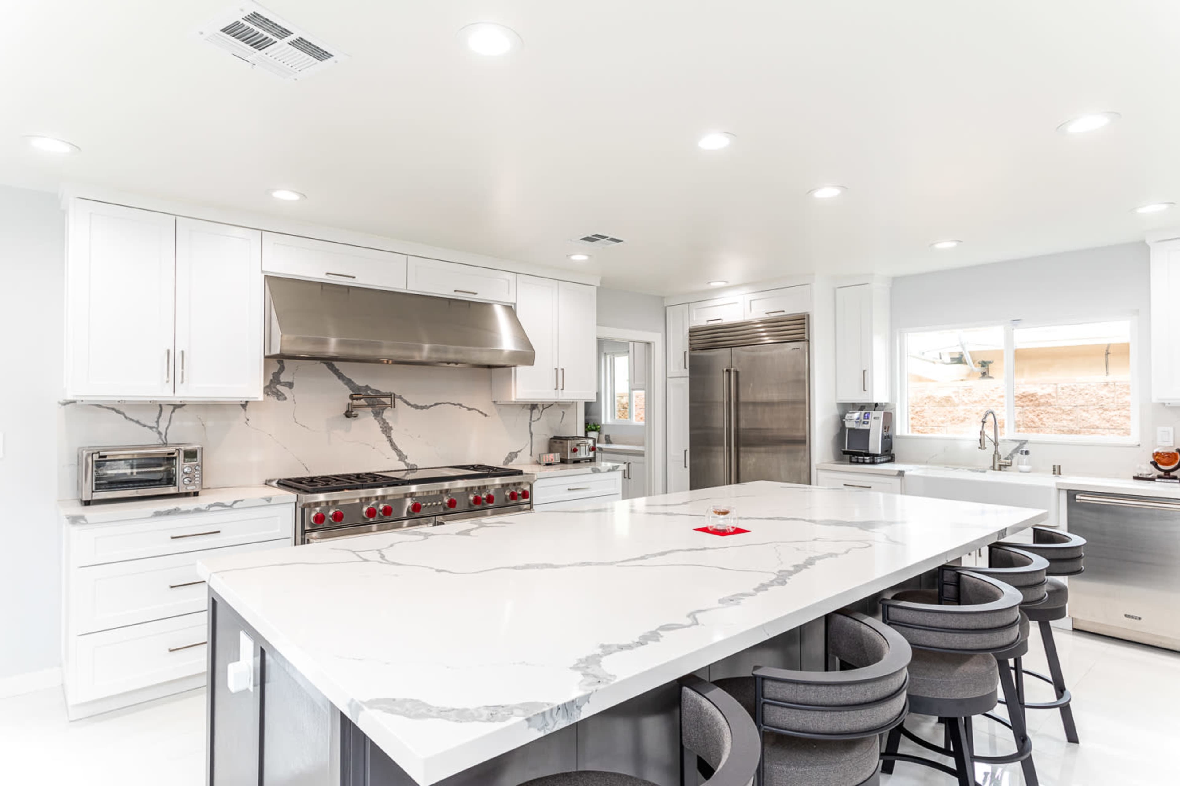 A modern kitchen with white cabinetry, a large island featuring a marble countertop, and stainless steel appliances.