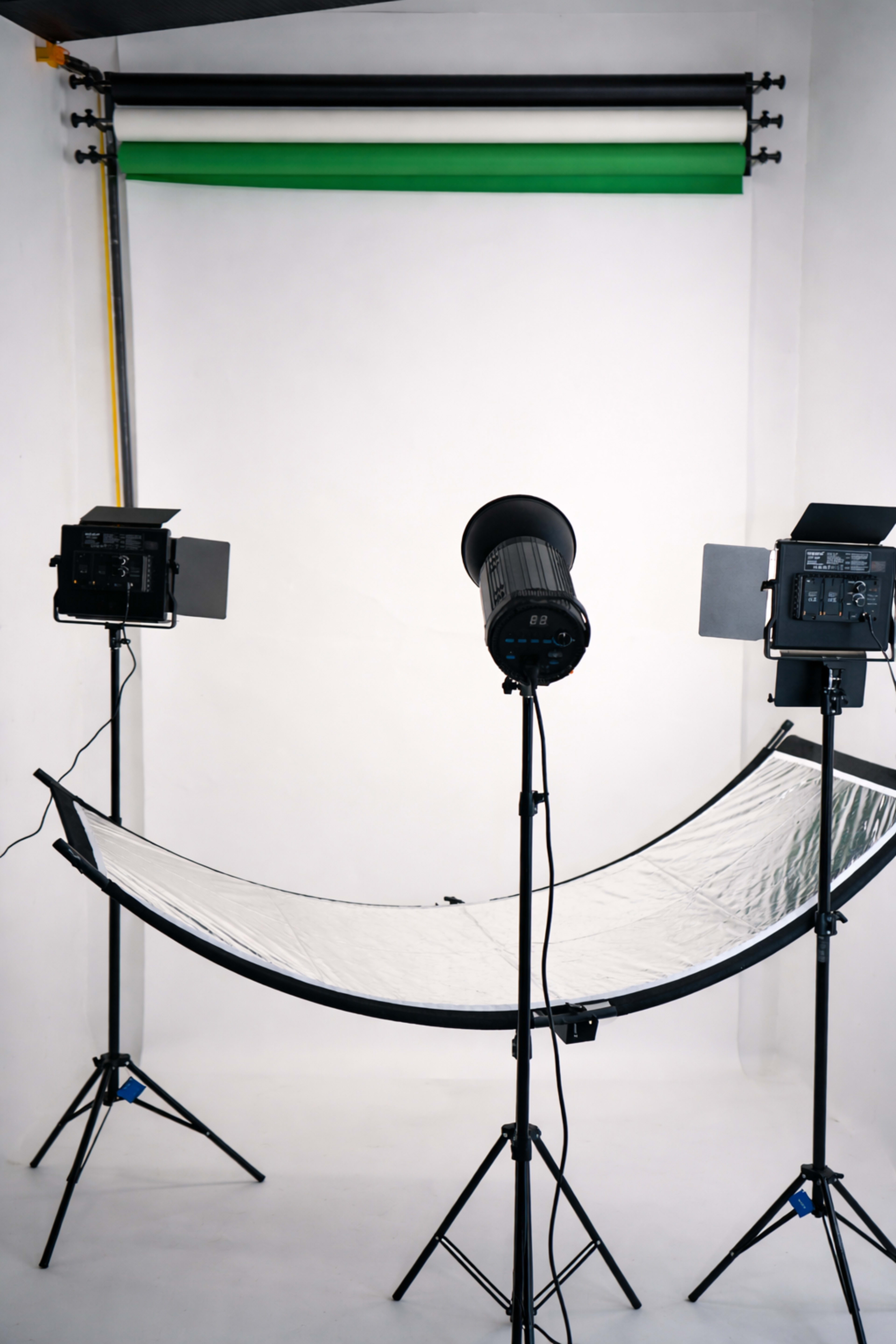 The image shows a photography studio setup with two light sources, a curved reflector, and a seamless backdrop.