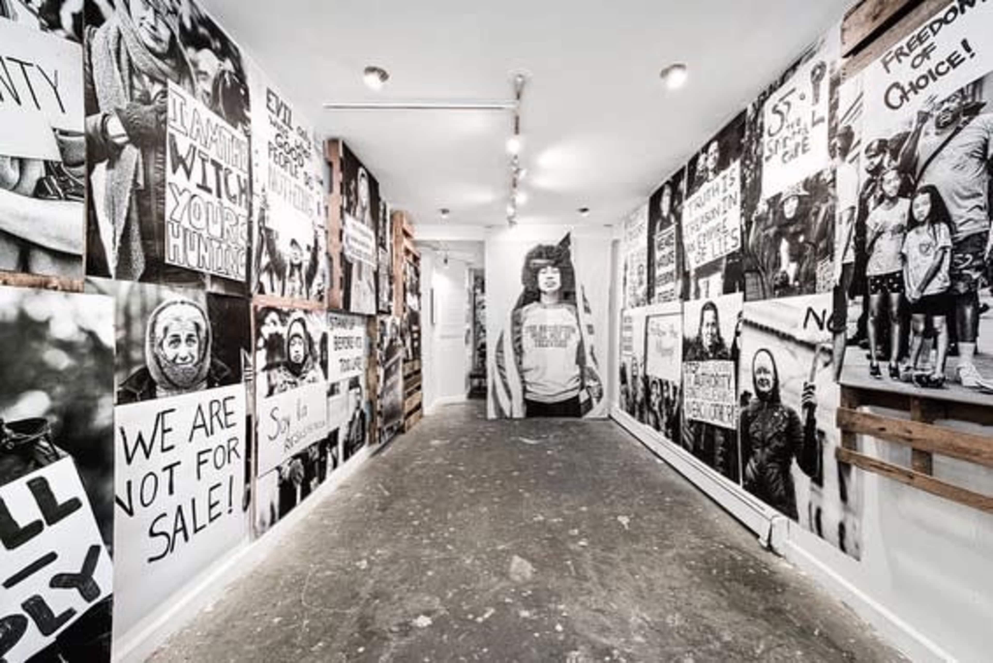 A narrow hallway lined with large black-and-white posters and murals depicting protest imagery and messages.