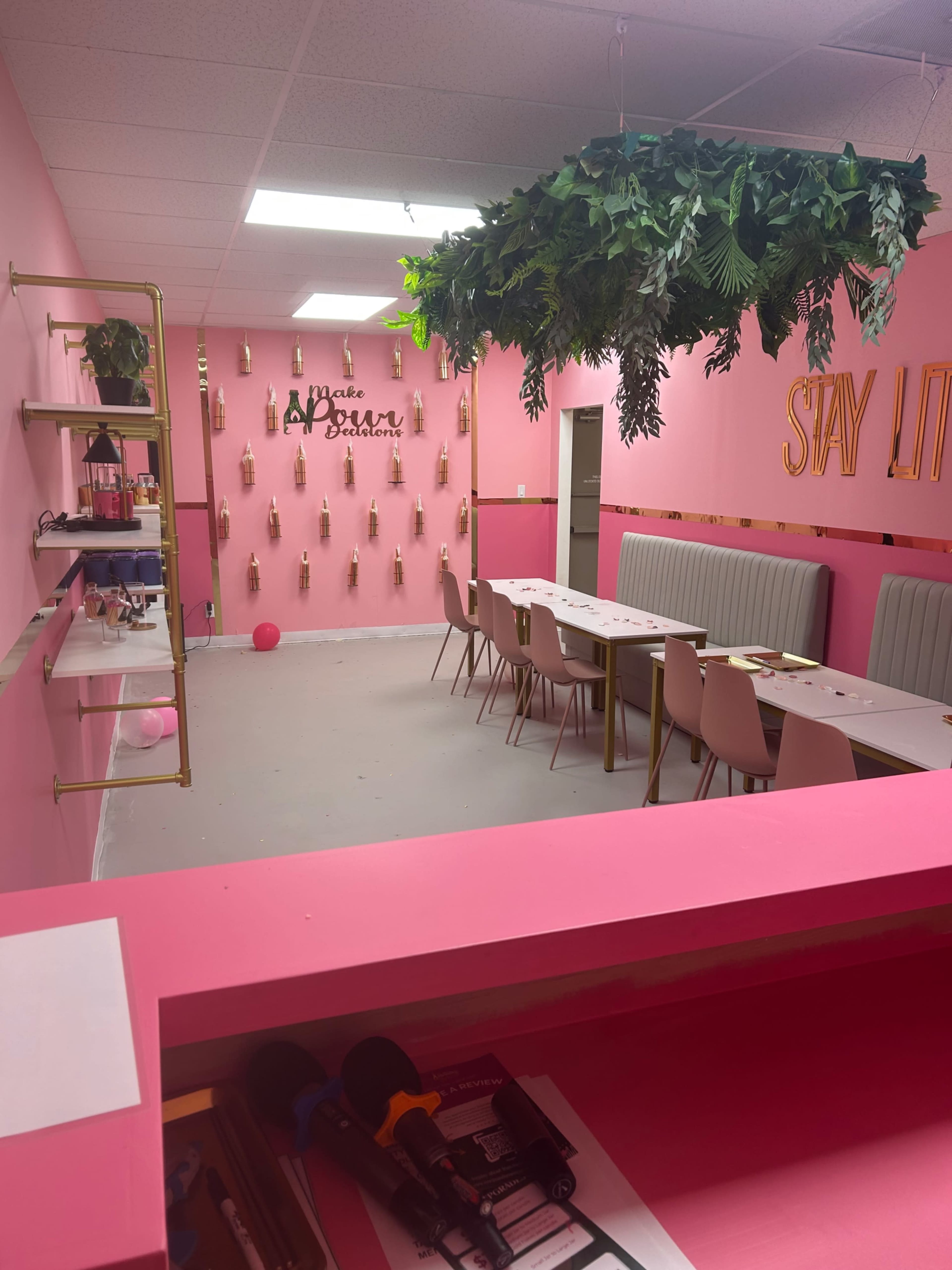 The image shows a pink-themed interior of a room with a long table set up, surrounded by chairs, and decorated with greenery and wall hangings.