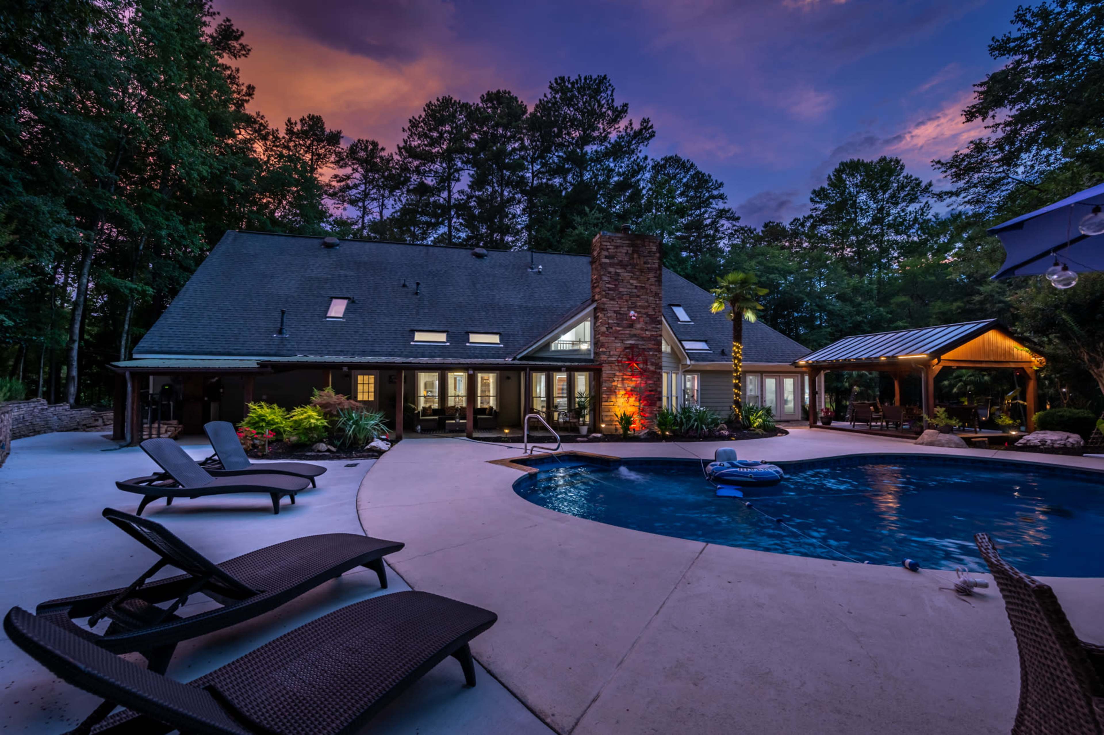A backyard scene features a swimming pool surrounded by lounge chairs, with a house and gazebo illuminated by sunset colors in the background.