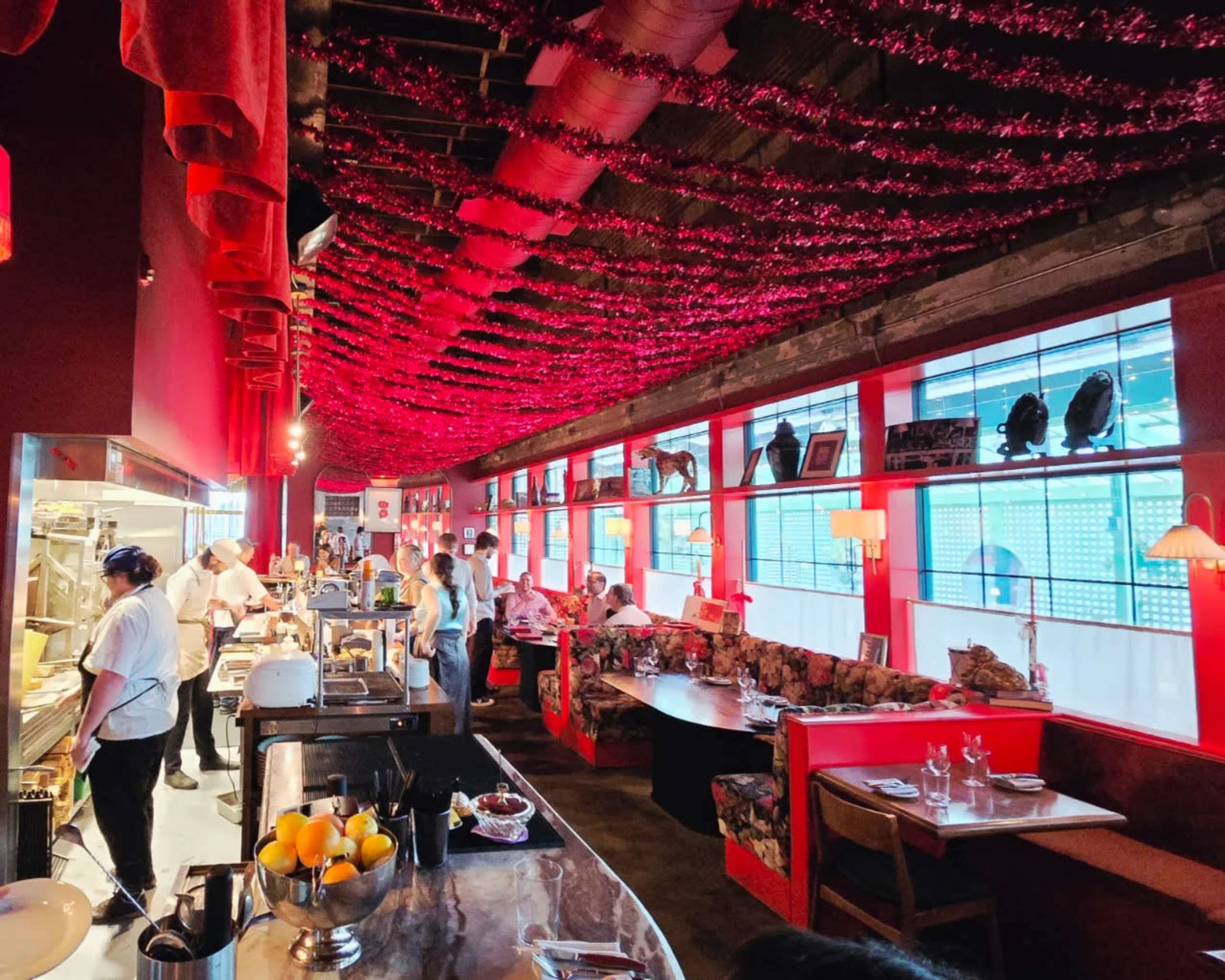 The image shows a vibrant restaurant interior with red decorations, a long counter, and diners seated at tables along the walls.