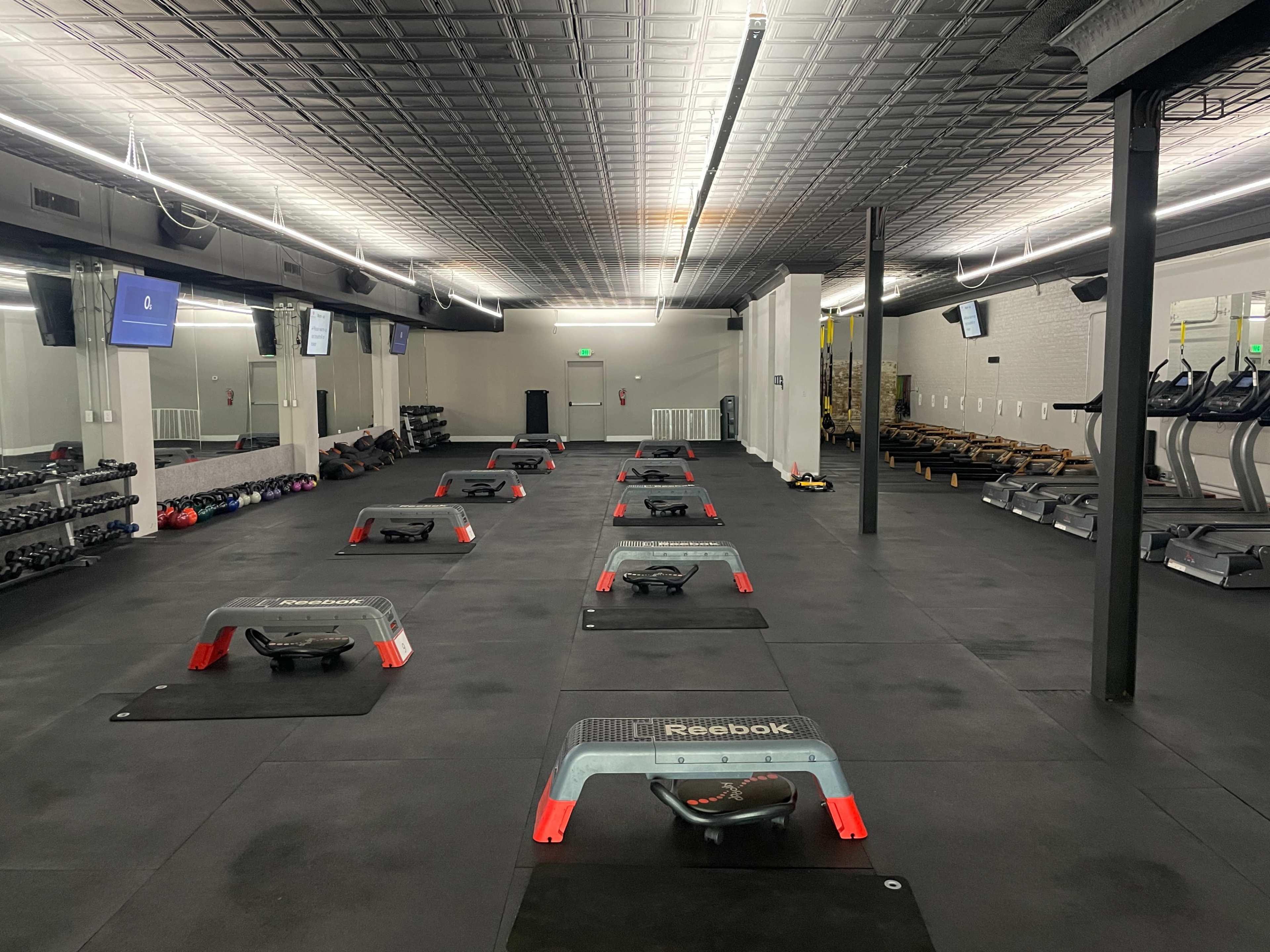 An empty gym with multiple exercise stations set up on a black rubber floor, along with various gym equipment including dumbbells and treadmills.