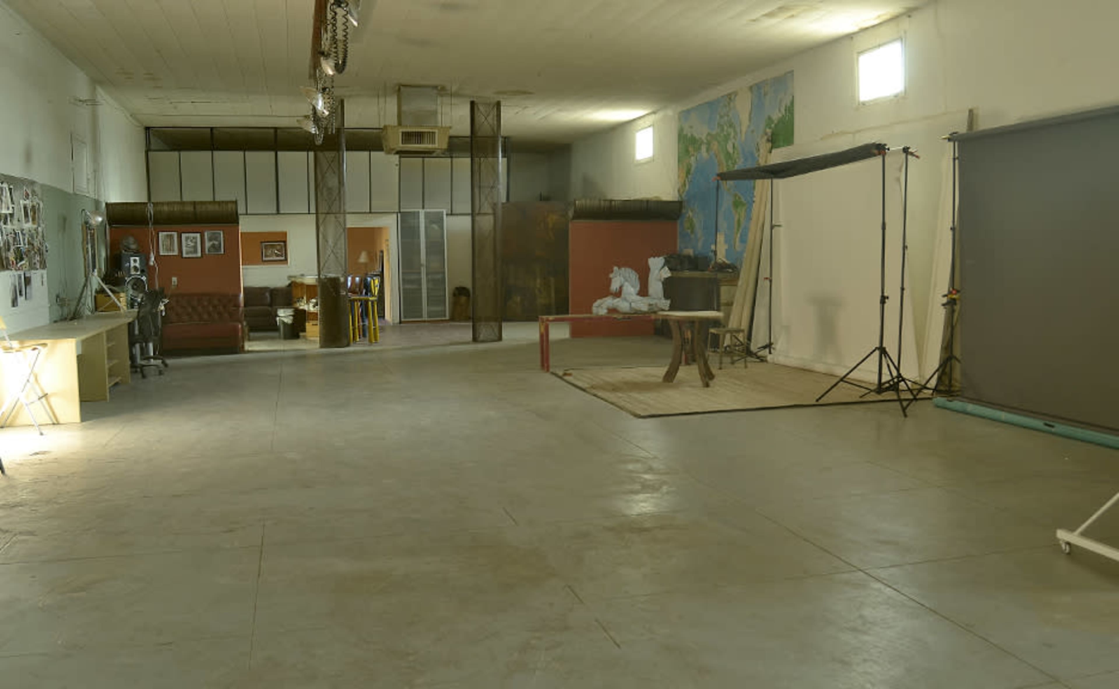 An empty art studio with a concrete floor, overhead lighting, and walls decorated with maps and photographs.