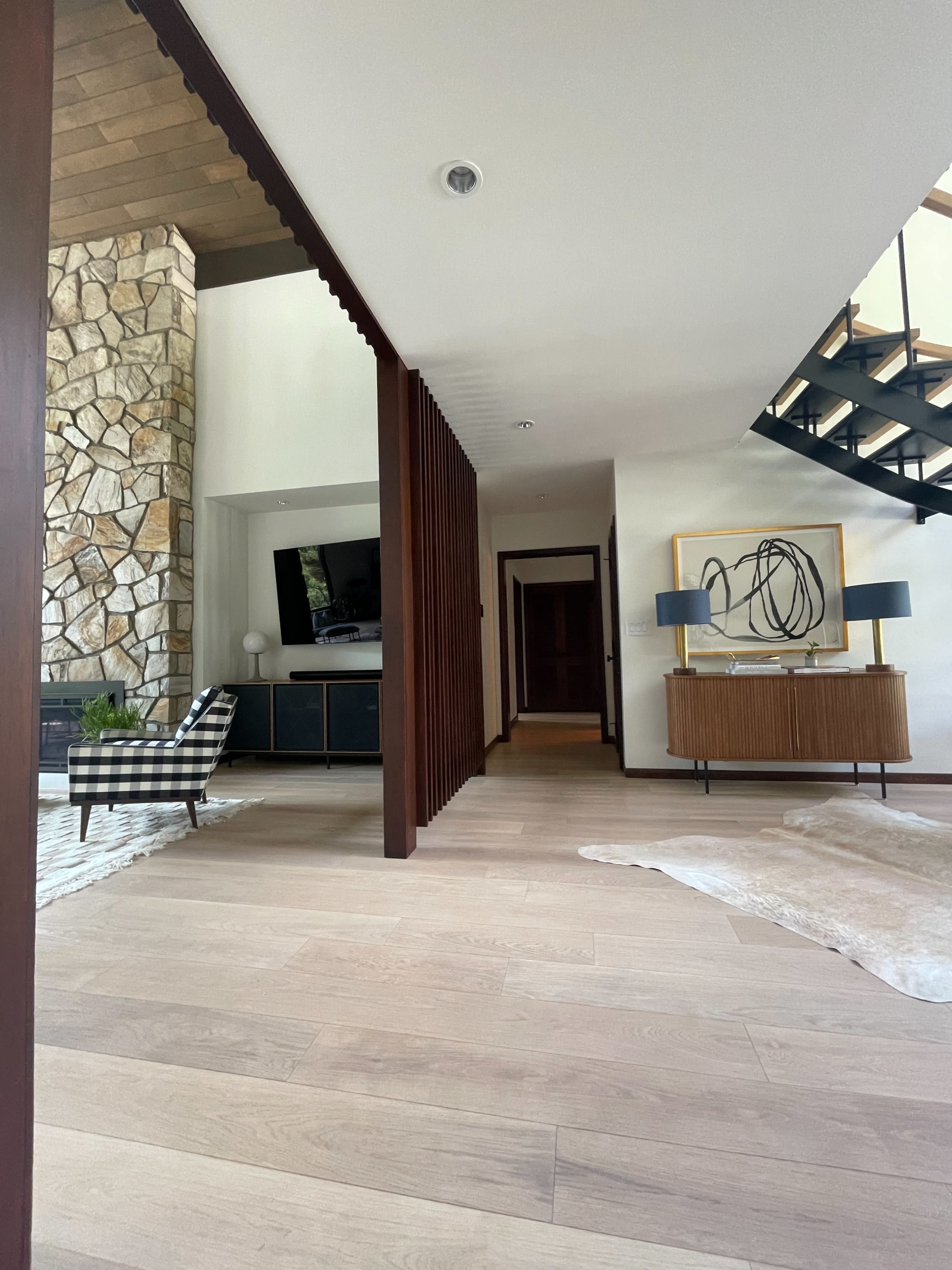The image shows a modern living space featuring a stone wall, a staircase, and a combination of wooden furniture and decor.