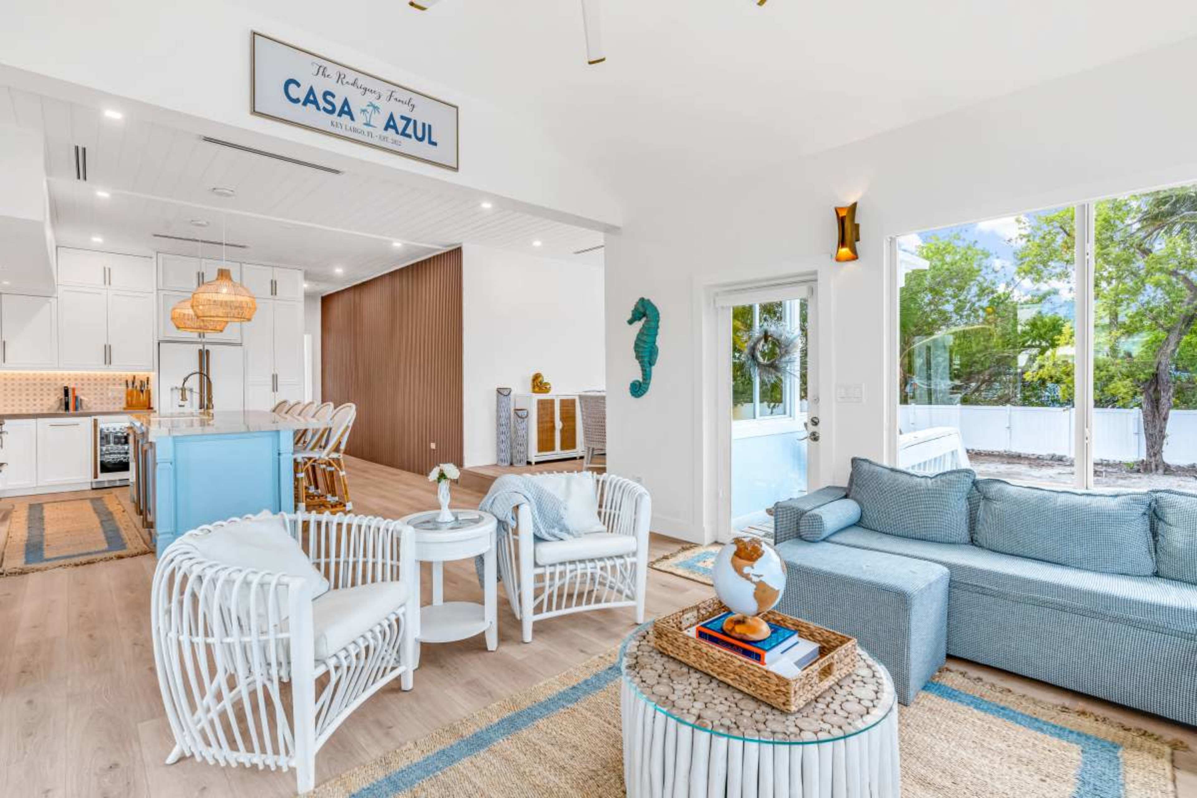 A bright living space features a light blue sofa, wicker chairs, and a large window that lets in natural light.