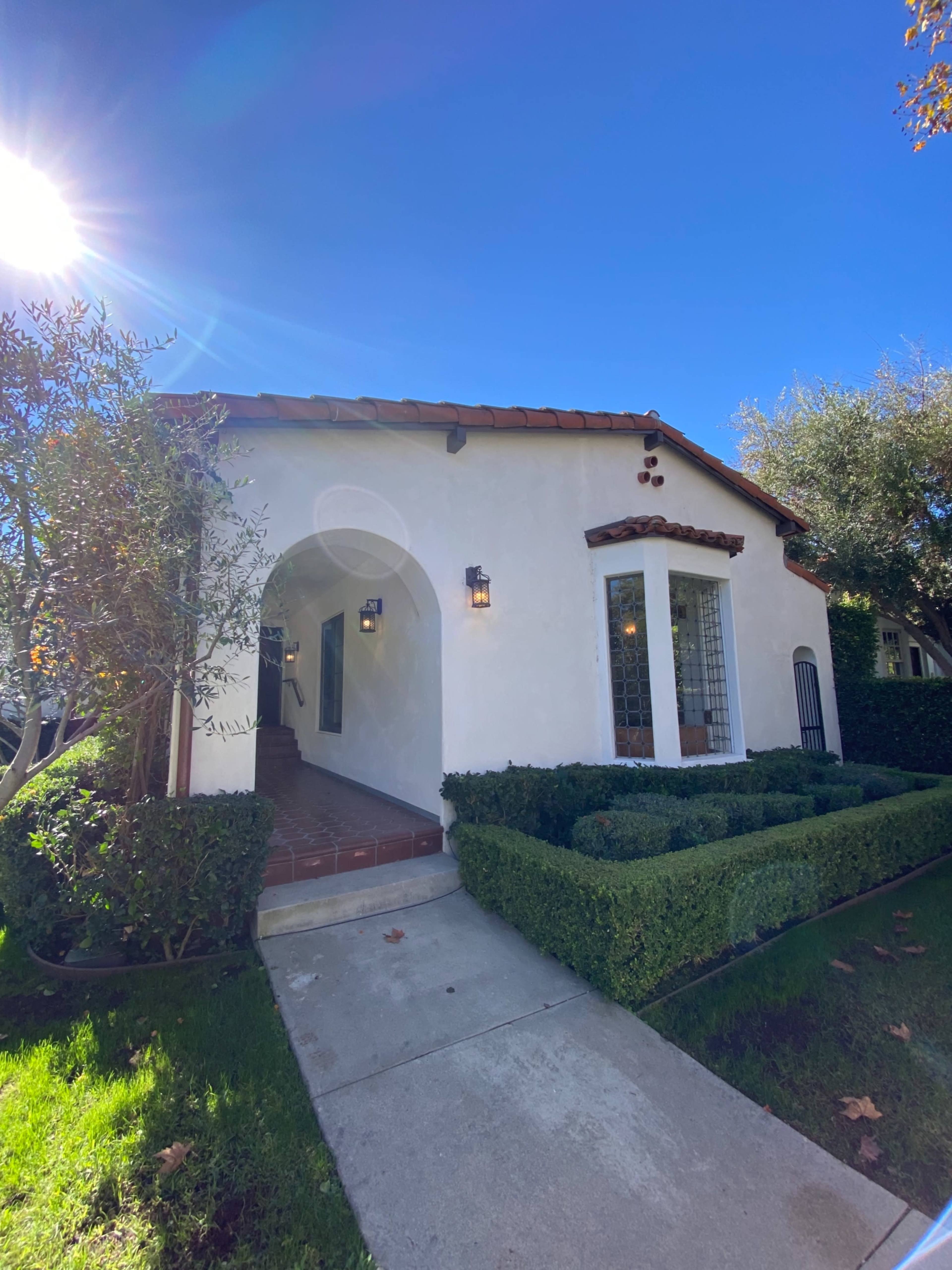 A white stucco house with a red tile roof and a neatly landscaped front yard featuring hedges and a pathway.