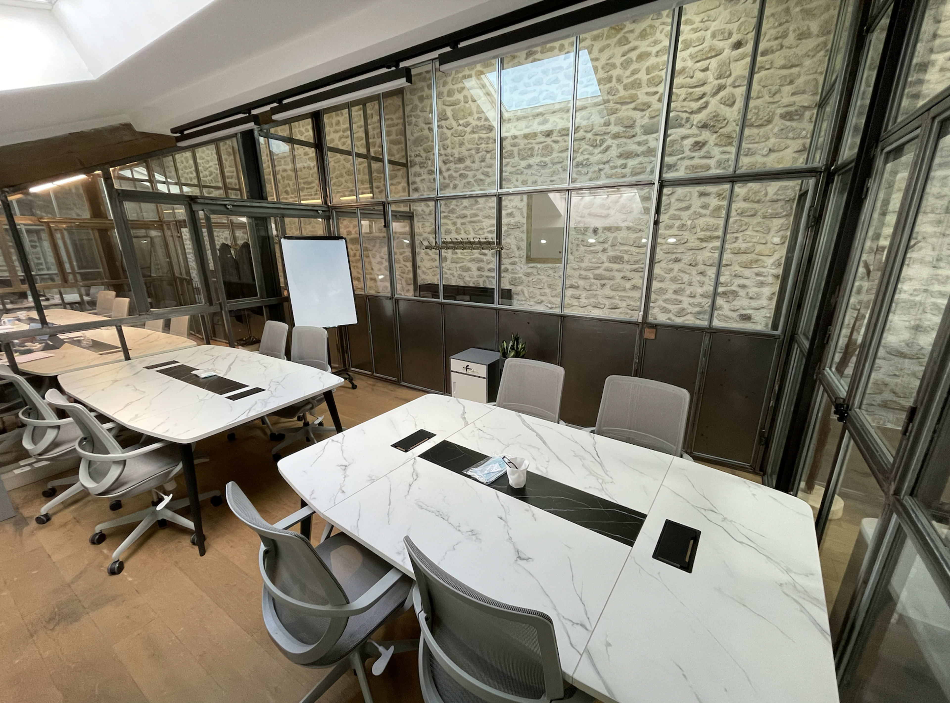 A modern conference room with large marble-topped tables, ergonomic chairs, and glass walls featuring exposed stone.