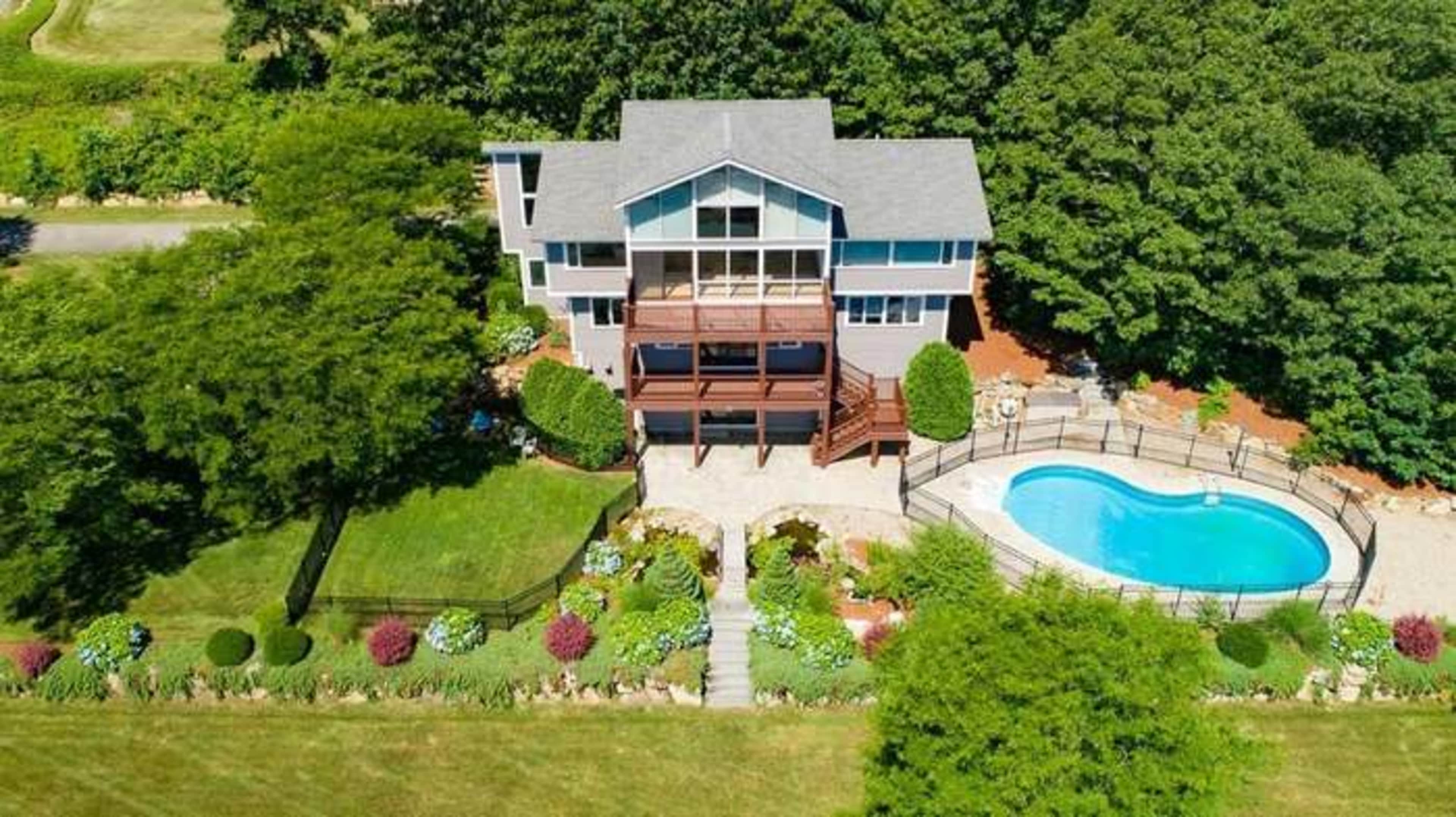 An aerial view of a large house with multiple levels, a deck, and a pool surrounded by a landscaped yard.