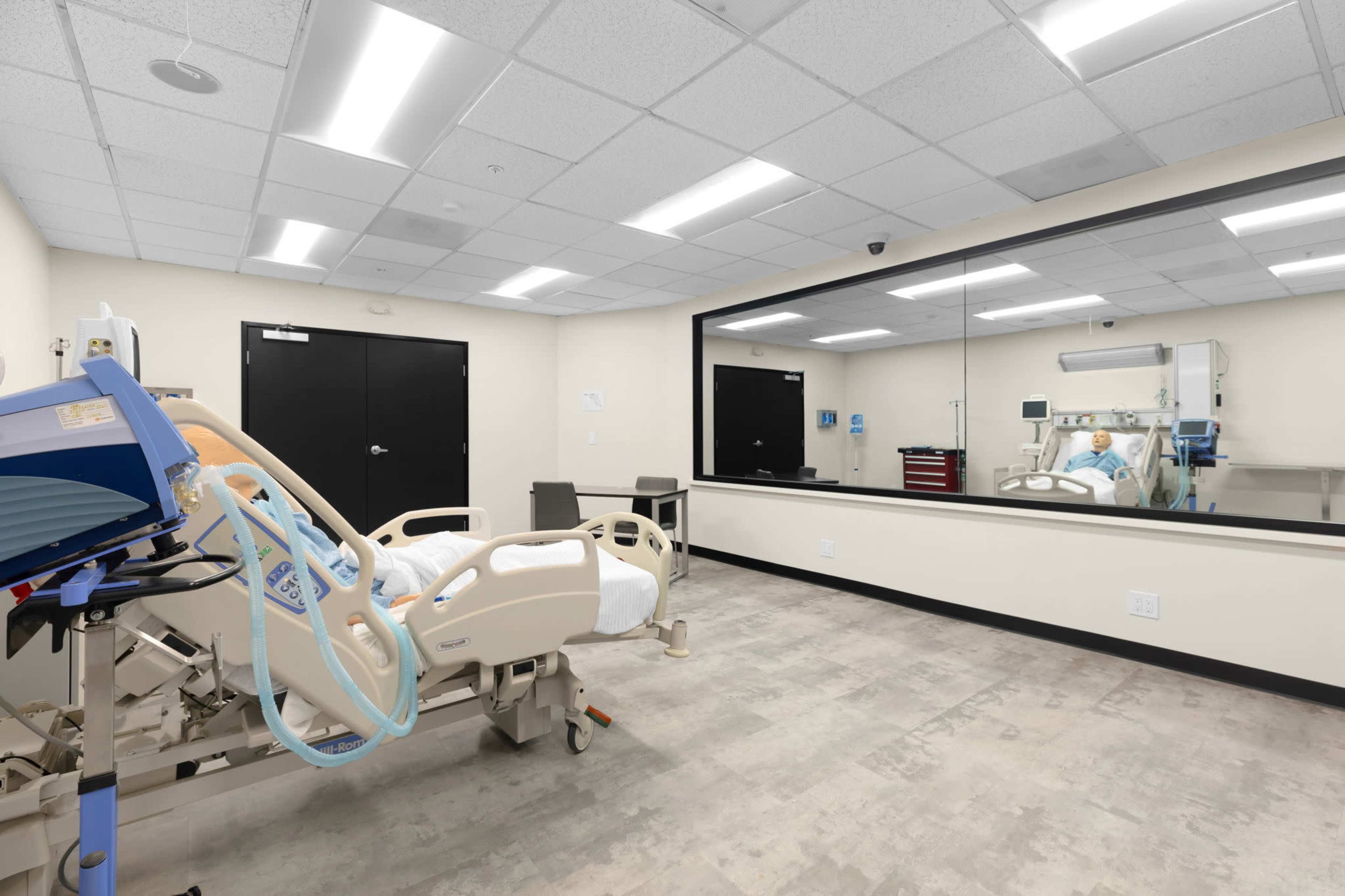 A hospital room with a patient's bed, medical equipment, and a large mirror reflecting a treatment area.