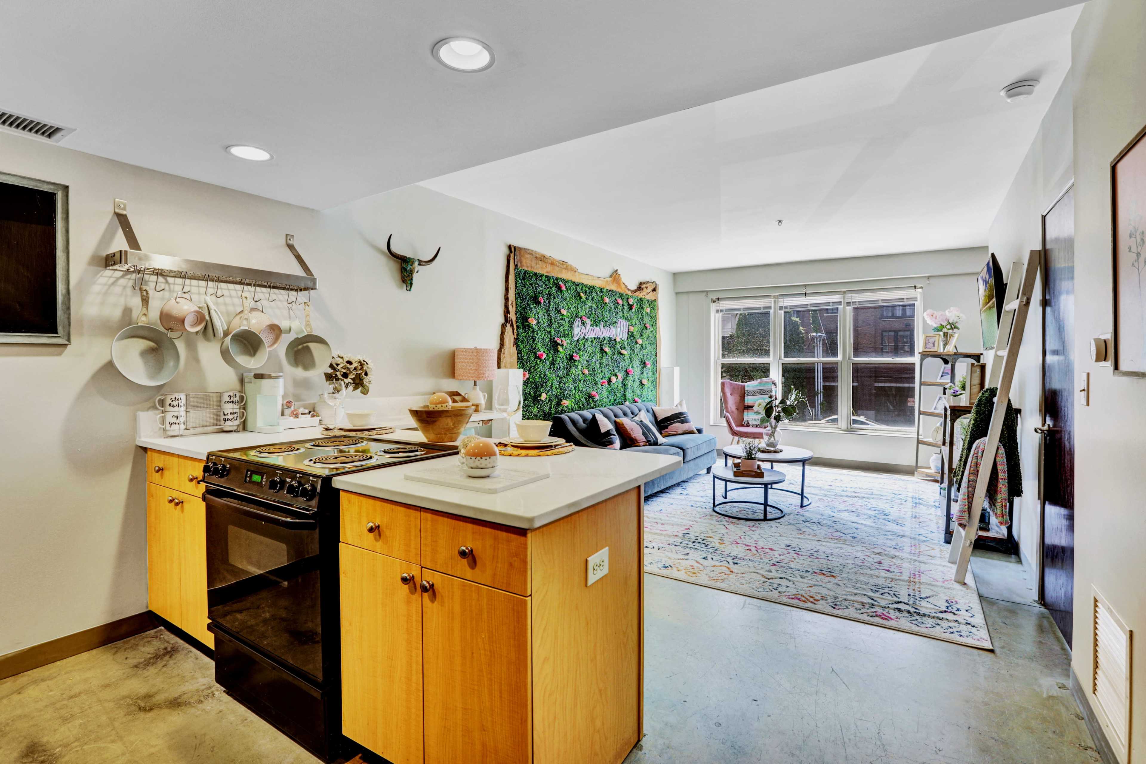 A modern kitchen and living area featuring a stove, a cozy seating arrangement, and a green plant wall decor.