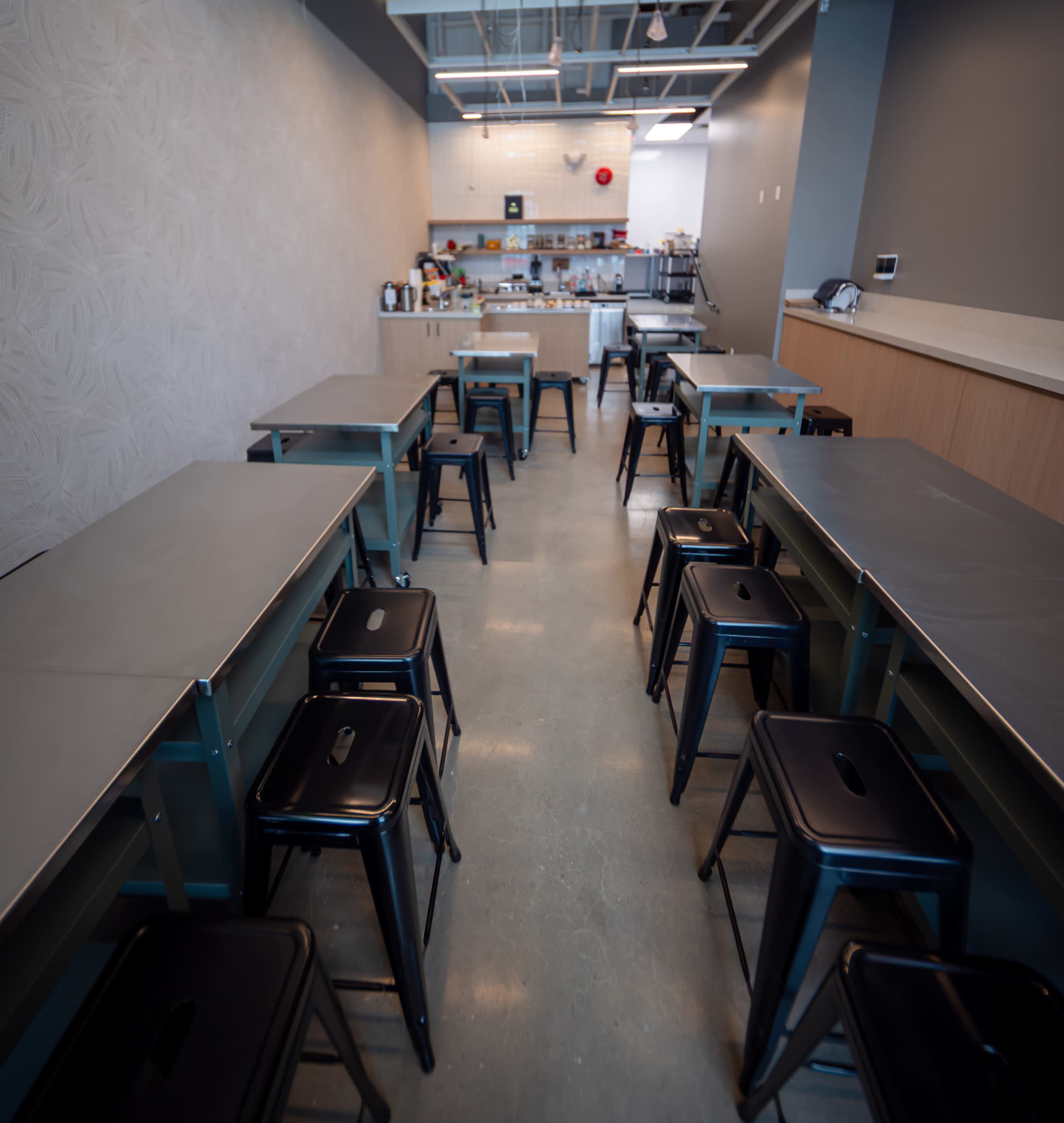 A spacious kitchen area features several tables and metal stools arranged in neat rows.