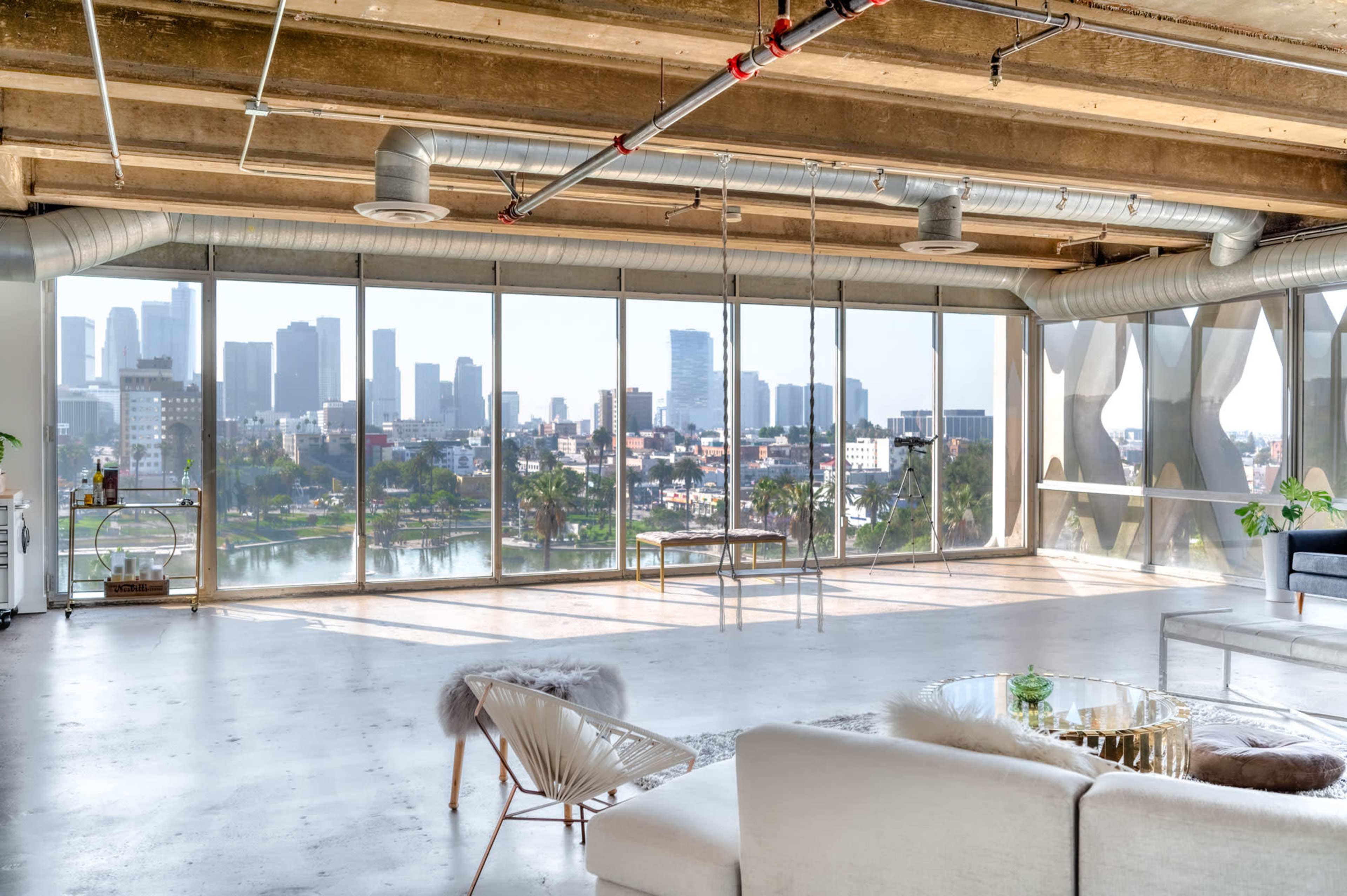 The image shows a modern, open interior space with large windows overlooking a city skyline and a body of water.