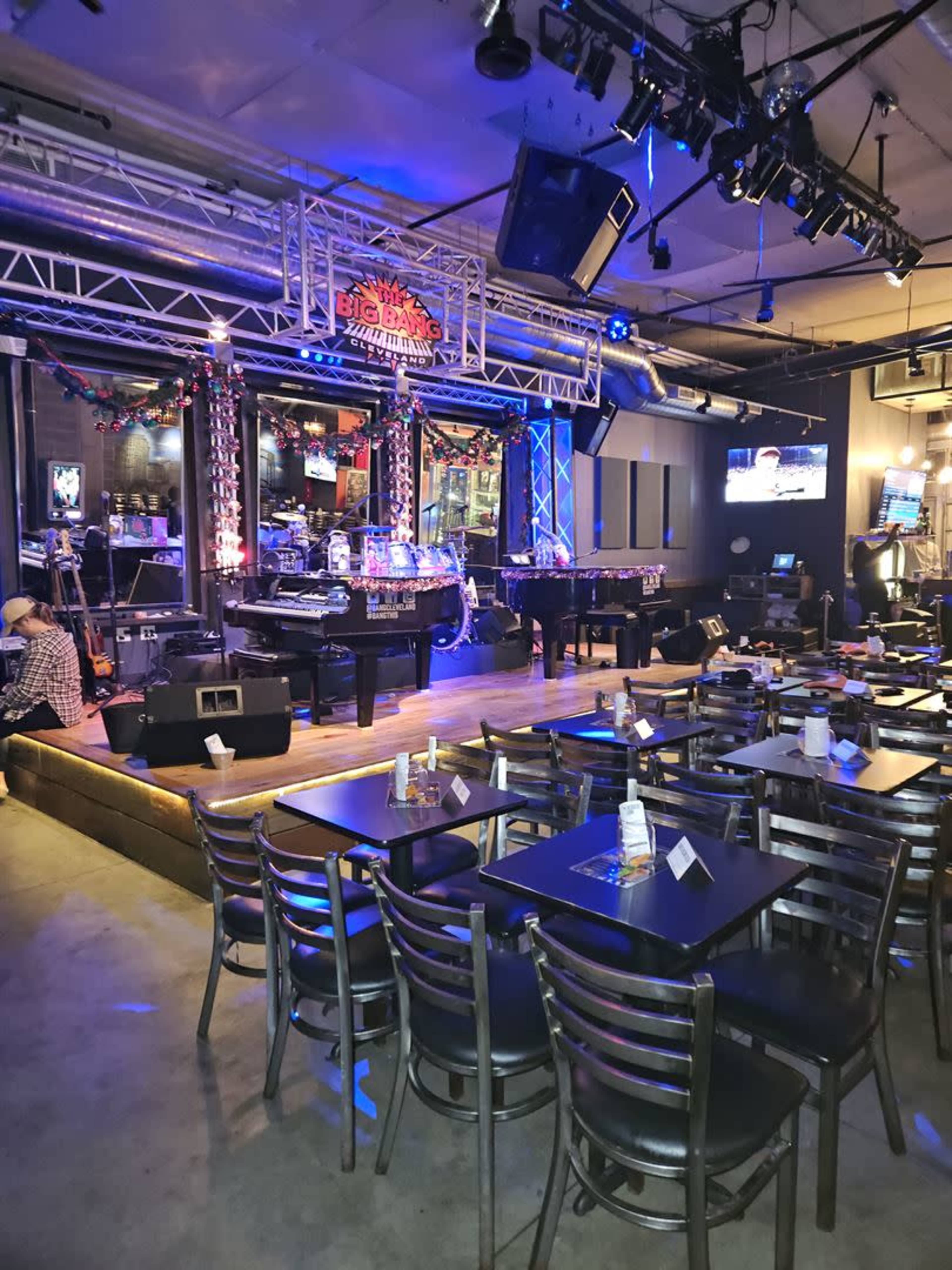 A live music venue with a stage, tables set for dining, and colorful lighting in the background.