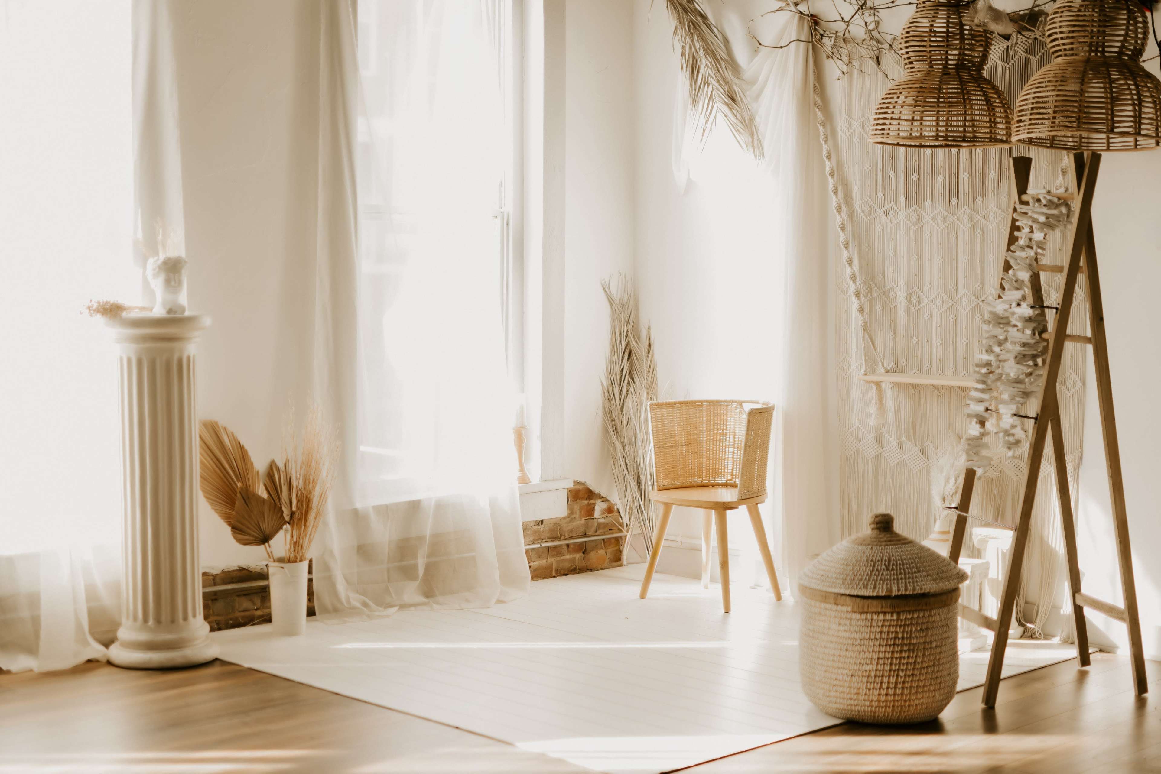 A bright, airy room features a wicker chair beside a window, decorated with plants and a woven storage basket.