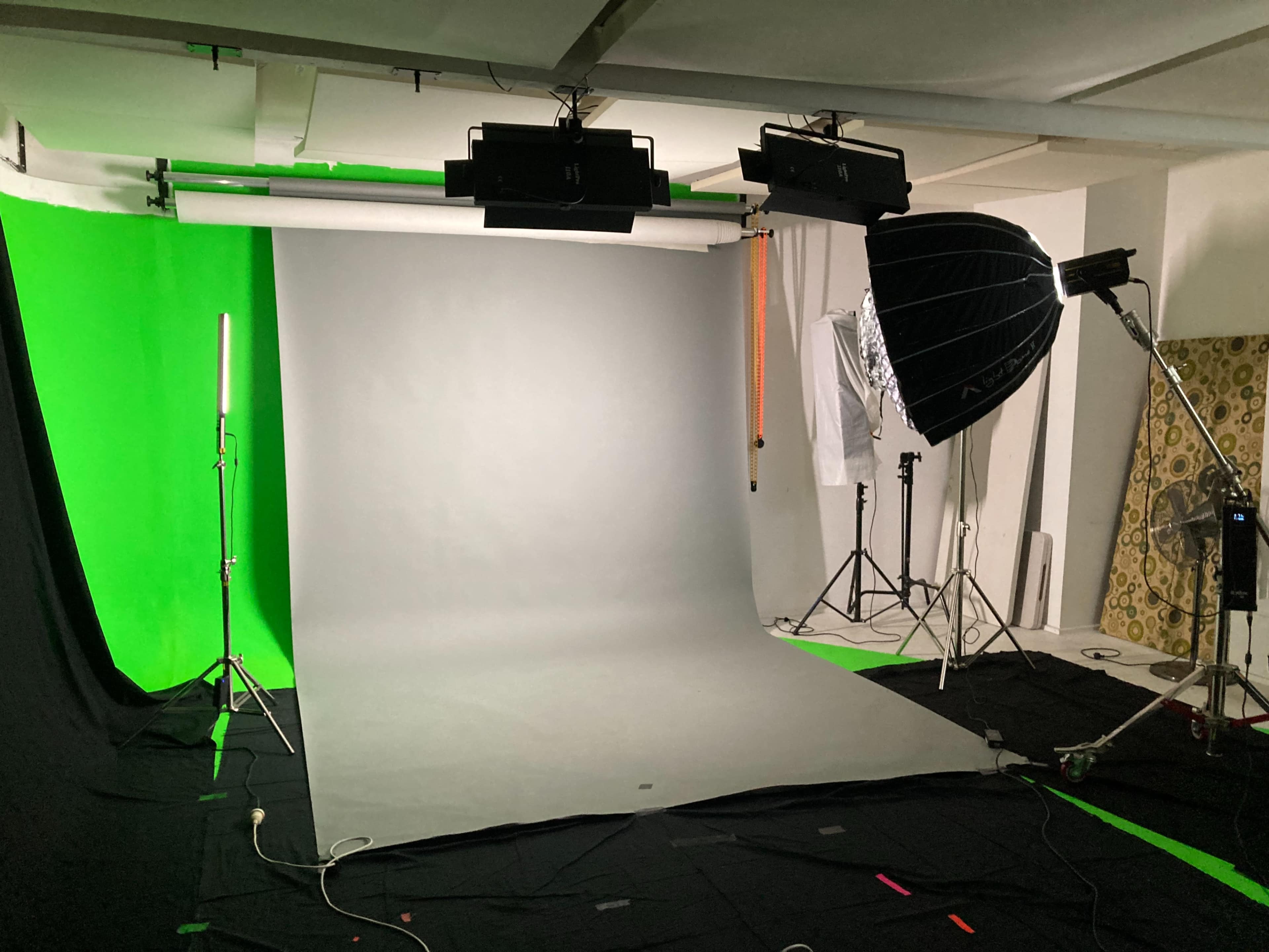 A photo studio equipped with a grey backdrop, green screen, and various lighting setups.