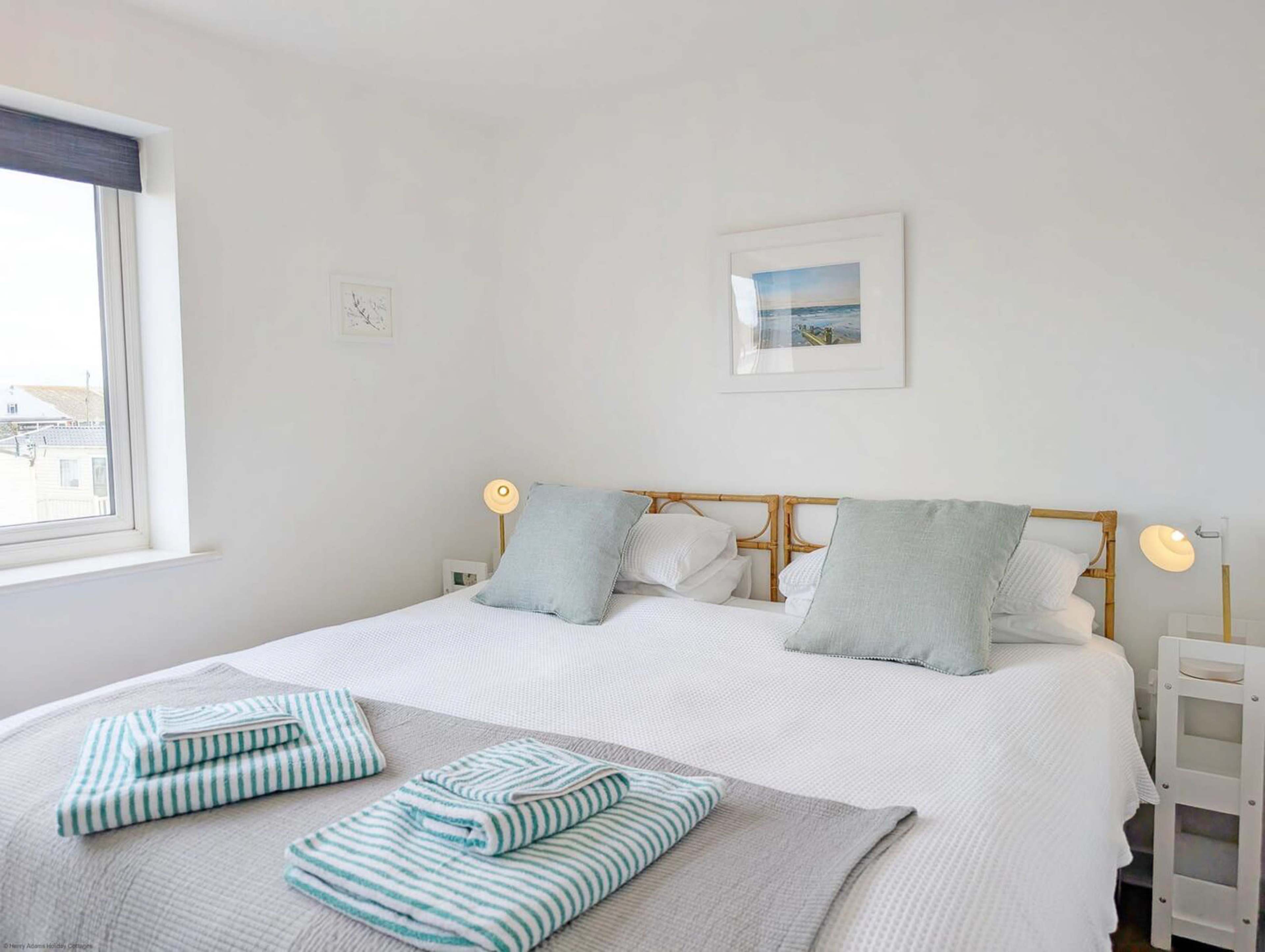 A neatly arranged bedroom features a double bed with light blue and white striped linens, two gray pillows, and a pair of bedside lamps.