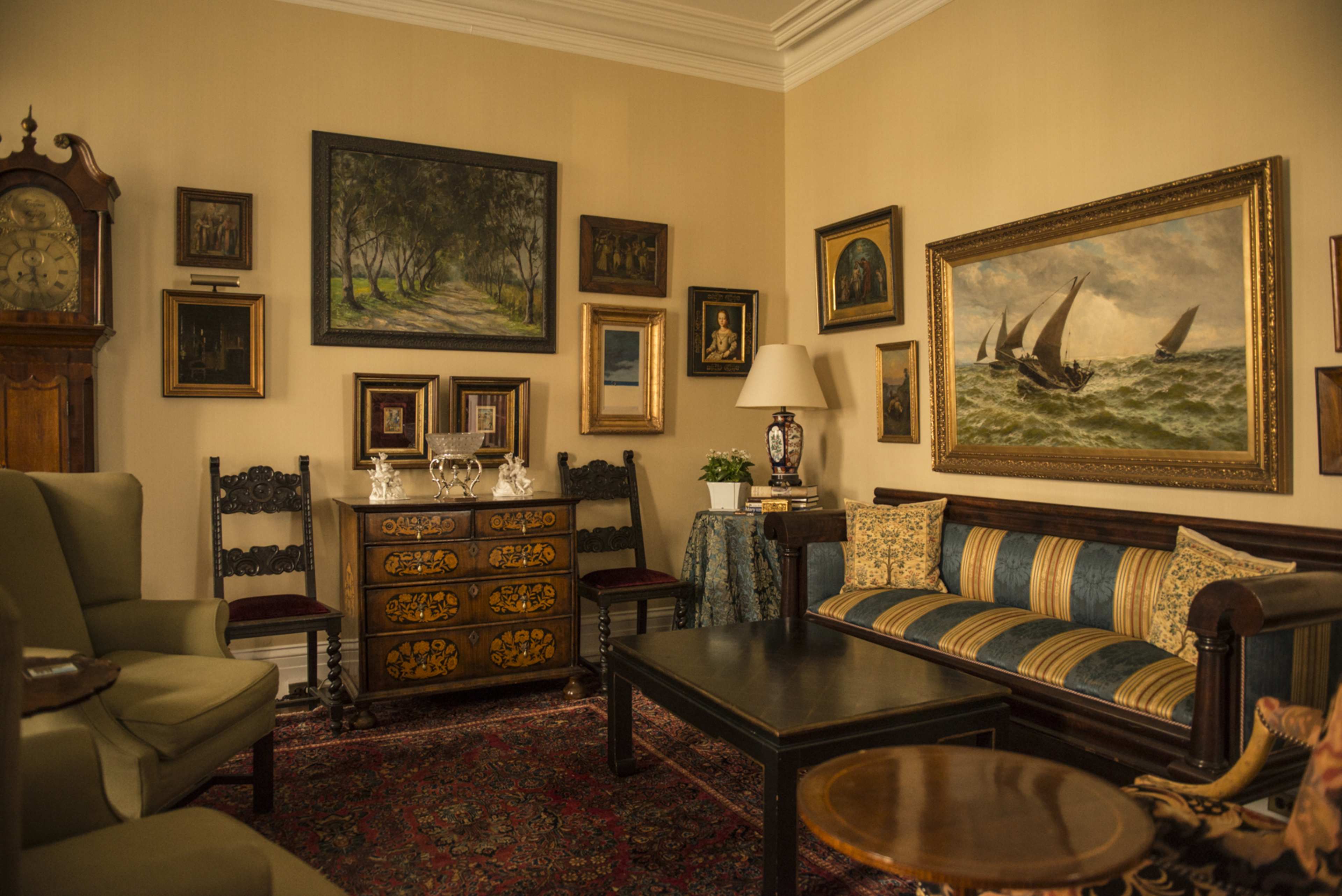 A vintage living room with ornate furniture, decorative paintings, and a large sideboard.