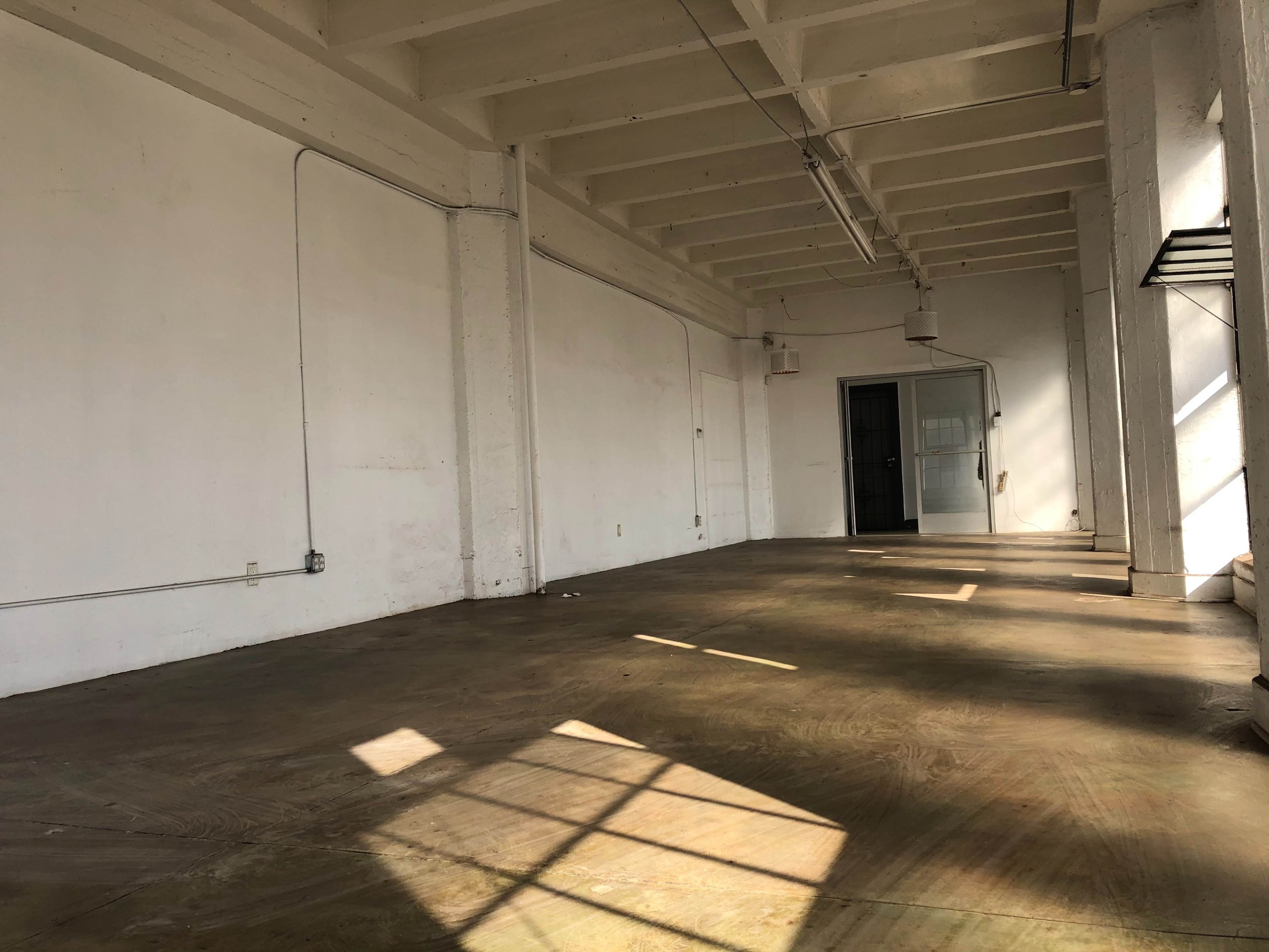 An empty, sunlit room with white walls and a concrete floor, featuring a doorway at the far end.