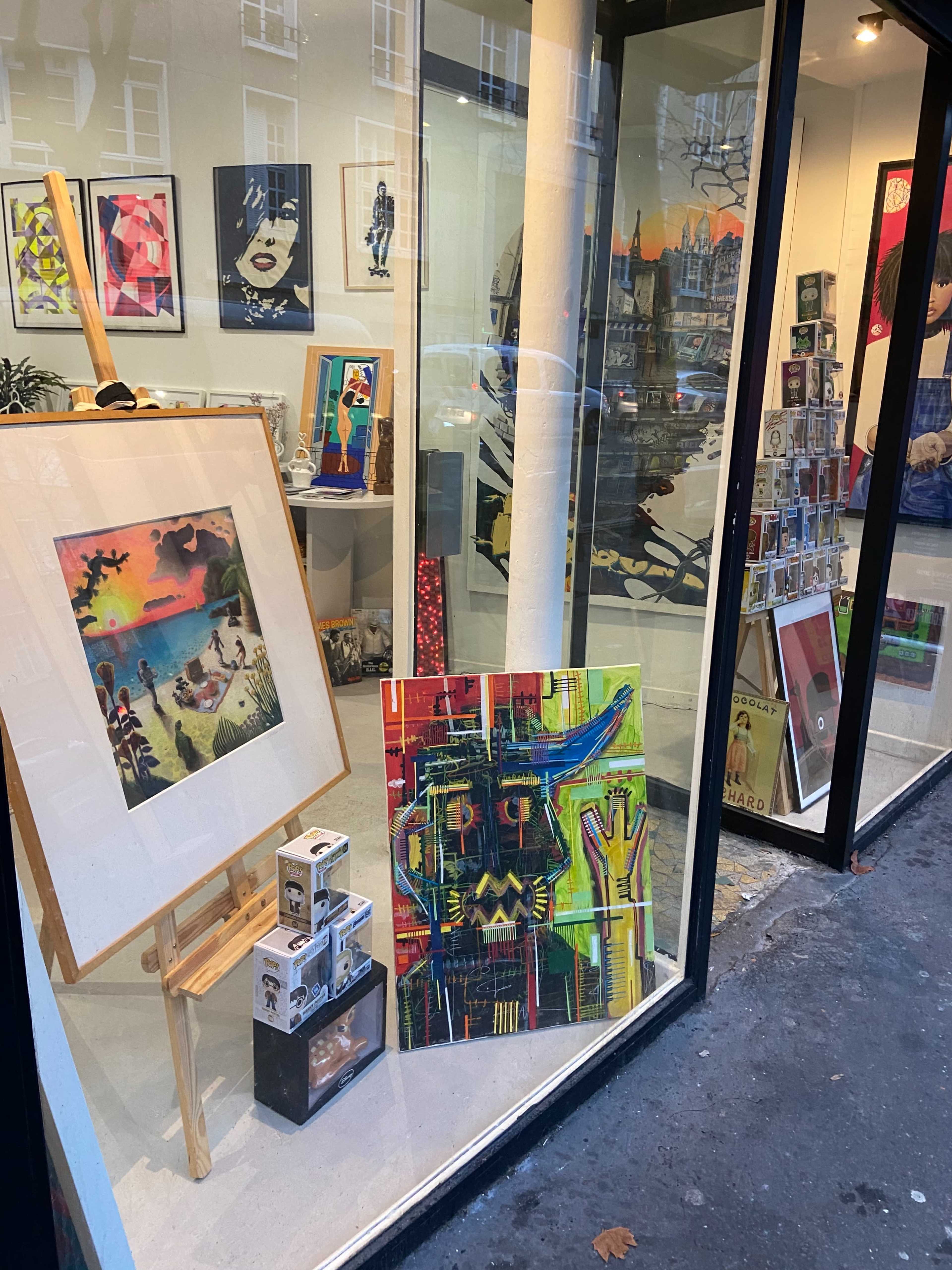An art gallery display featuring a variety of colorful paintings and framed artworks visible through a large window.