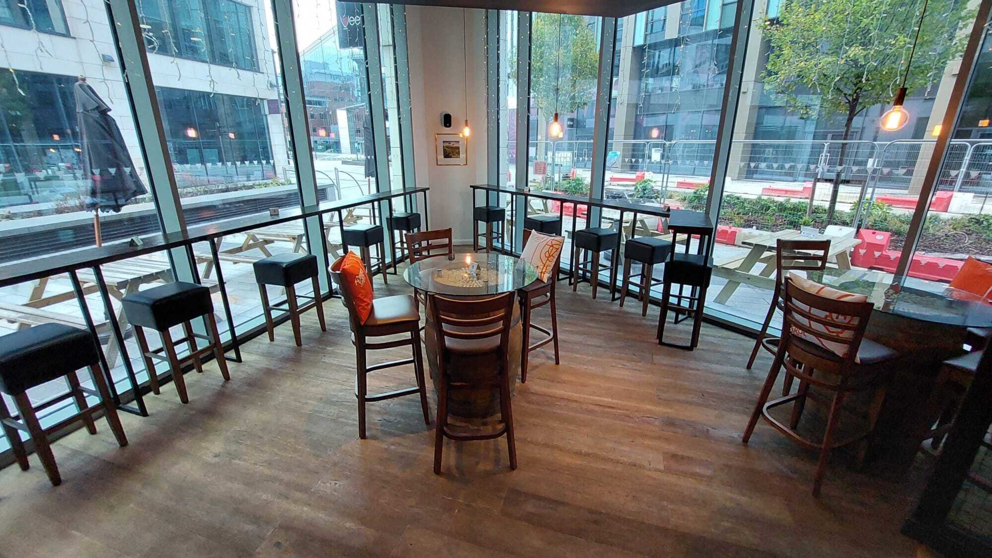 A modern café interior with tall chairs surrounding a circular glass table and large windows overlooking an outdoor space.