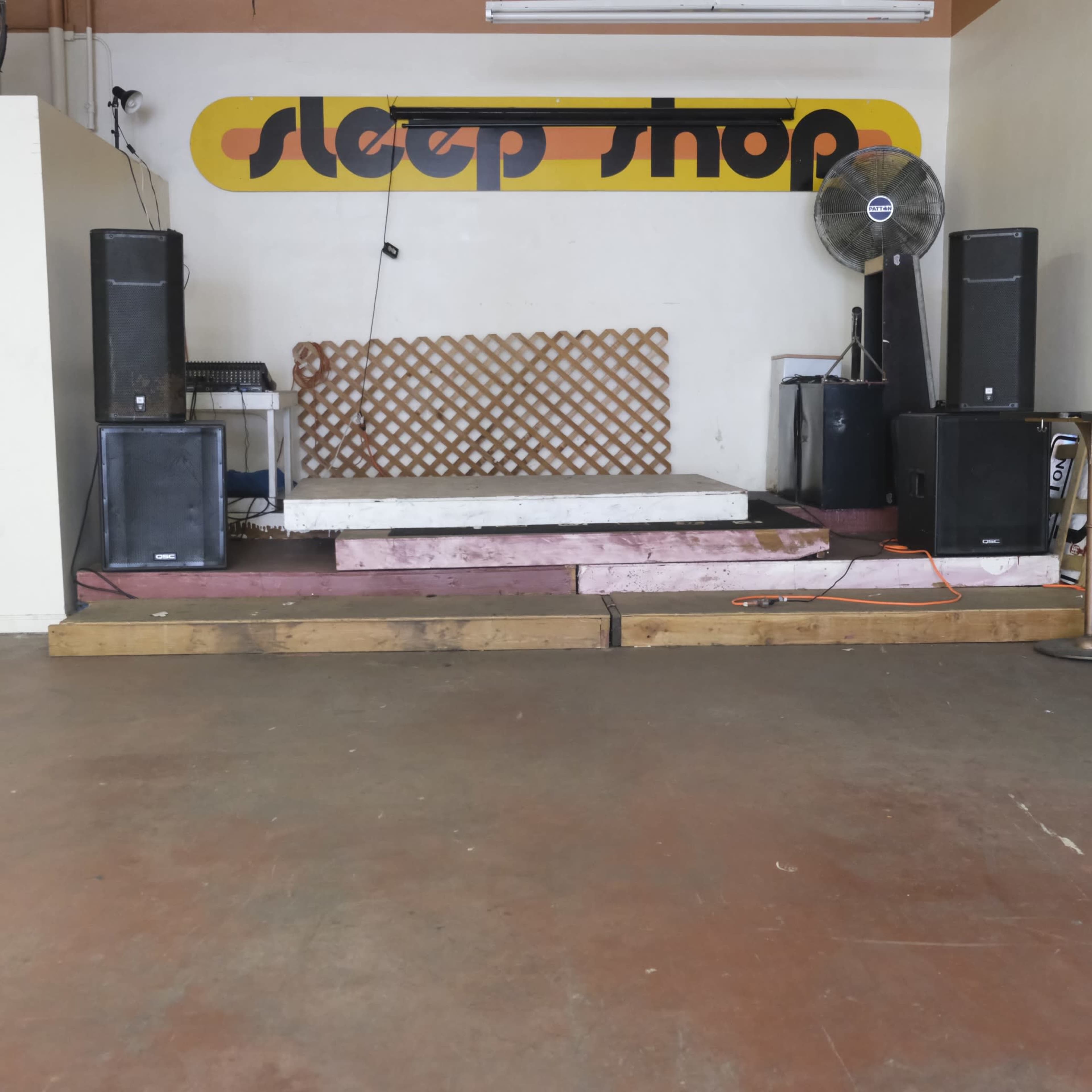 The image shows a stage area in a store named "sleep shop," featuring a raised platform, speaker systems on either side, and a lattice backdrop.