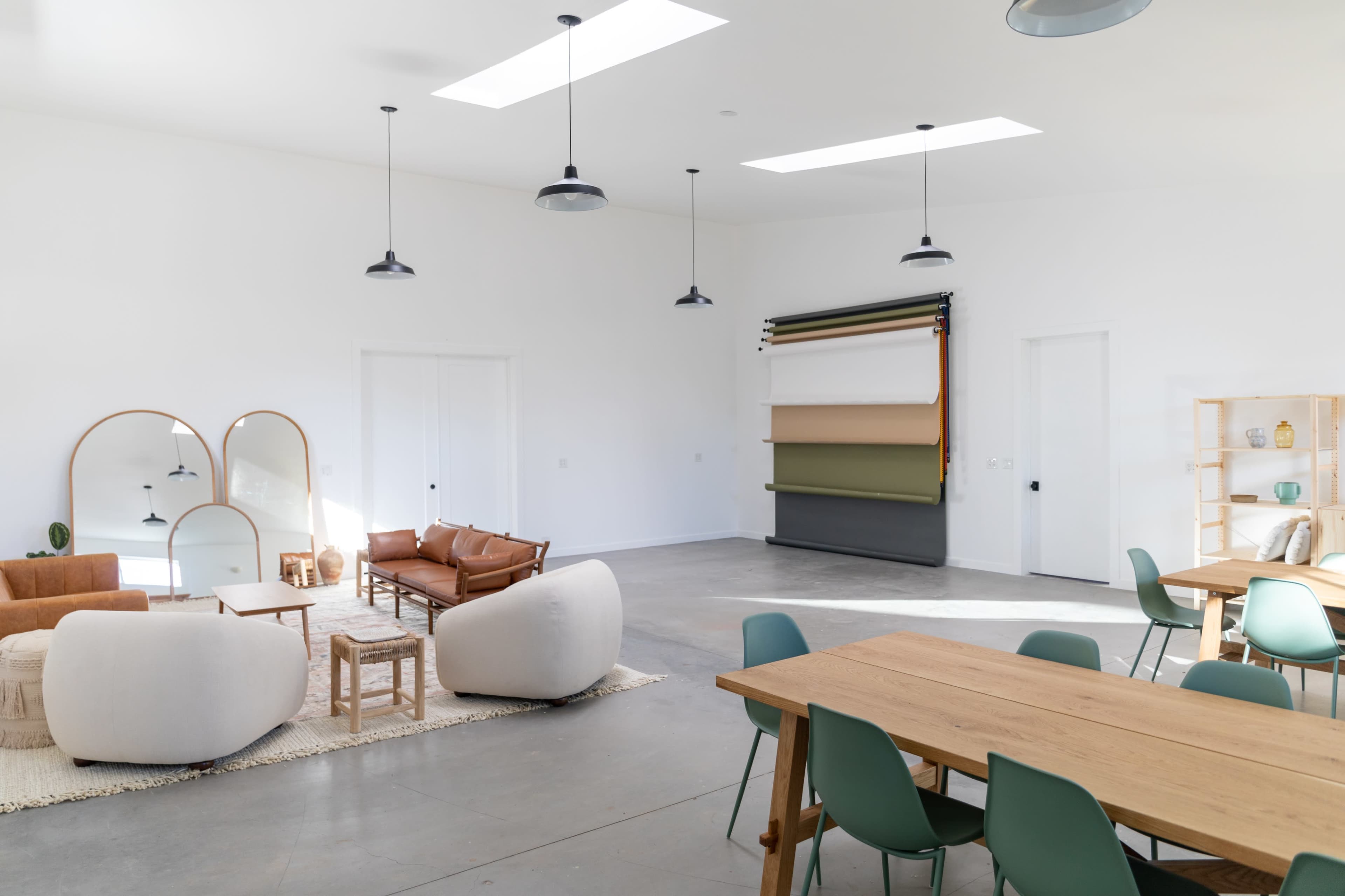 A modern, bright interior space featuring a seating area with sofas, a dining table, and a variety of decorative elements.