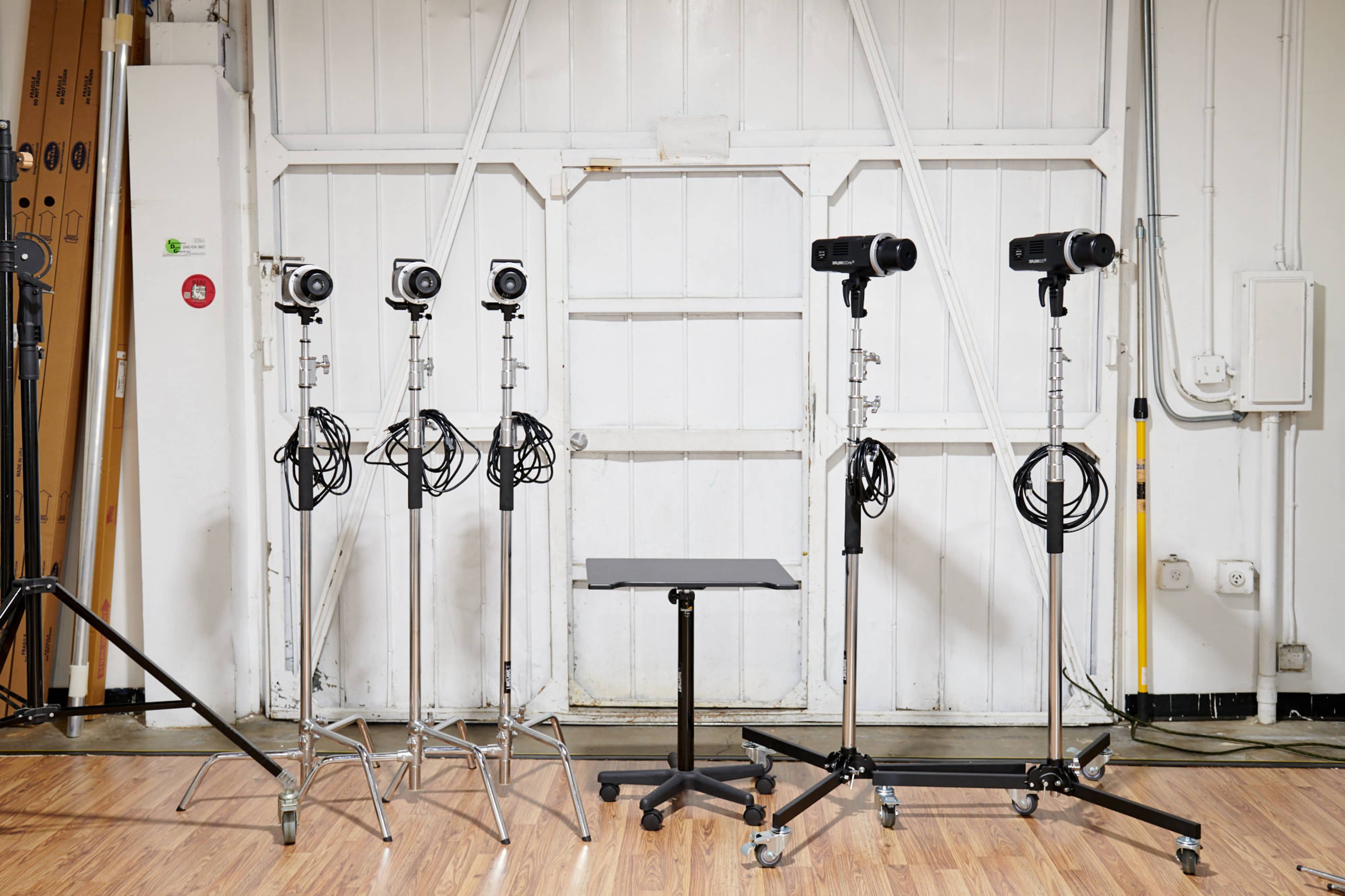 A row of four cameras mounted on stands and a small table placed in front of them against a white wall.