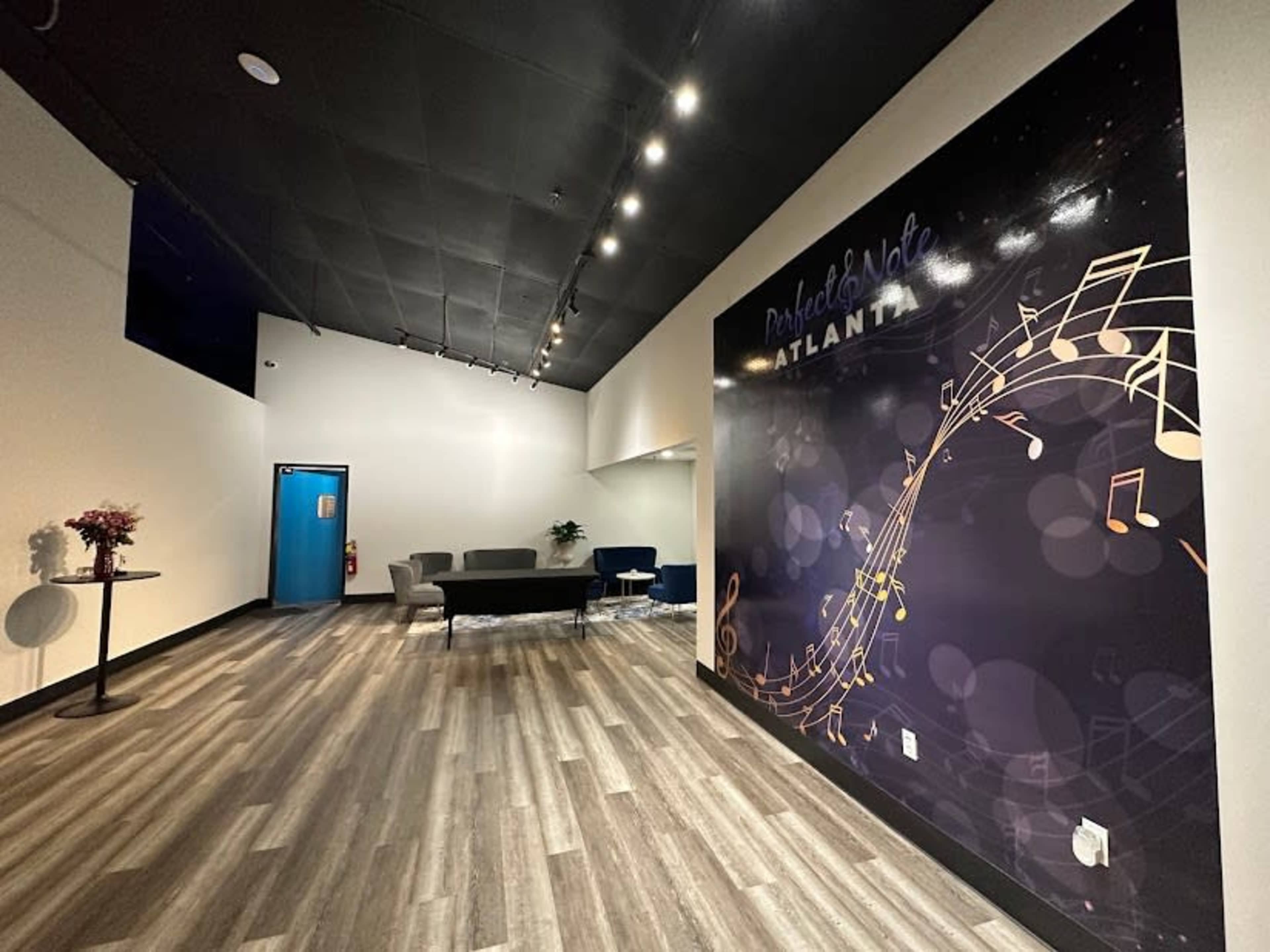 A spacious lobby featuring a dark wall with musical notes, a seating area with a gray sofa, and a blue door at the end of the room.