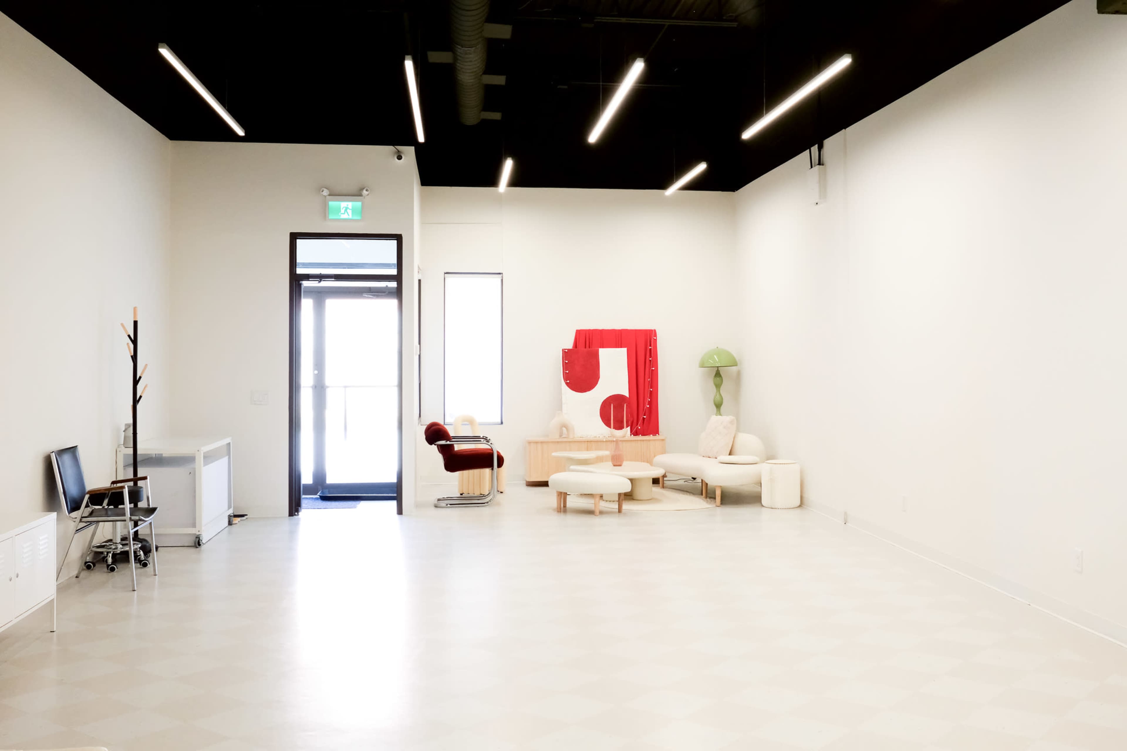 A spacious, minimalist interior featuring modern furniture, including a red sculpture and various seating arrangements, with large windows allowing natural light to enter.