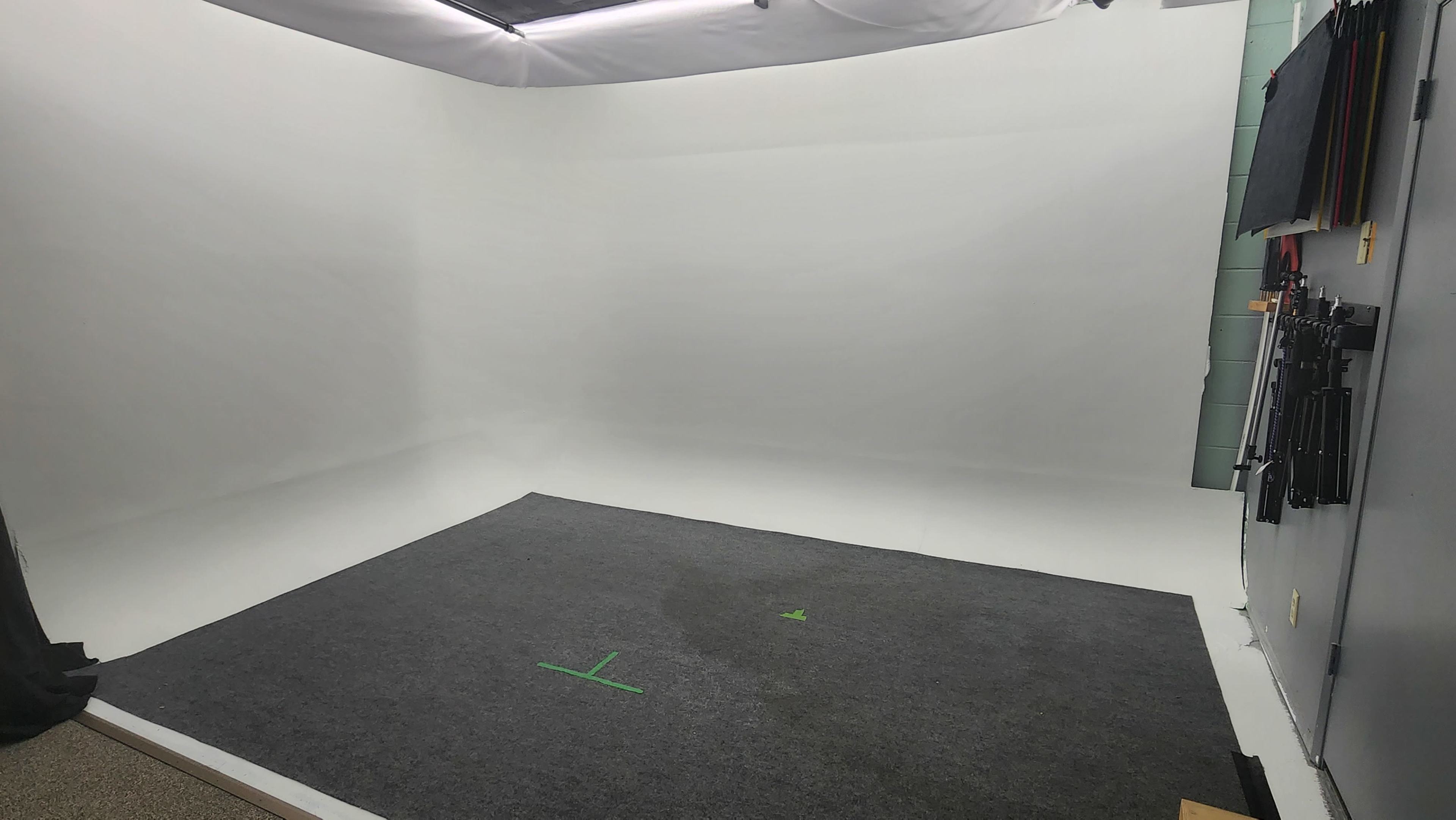 An empty studio space with a gray carpet and a seamless white backdrop.