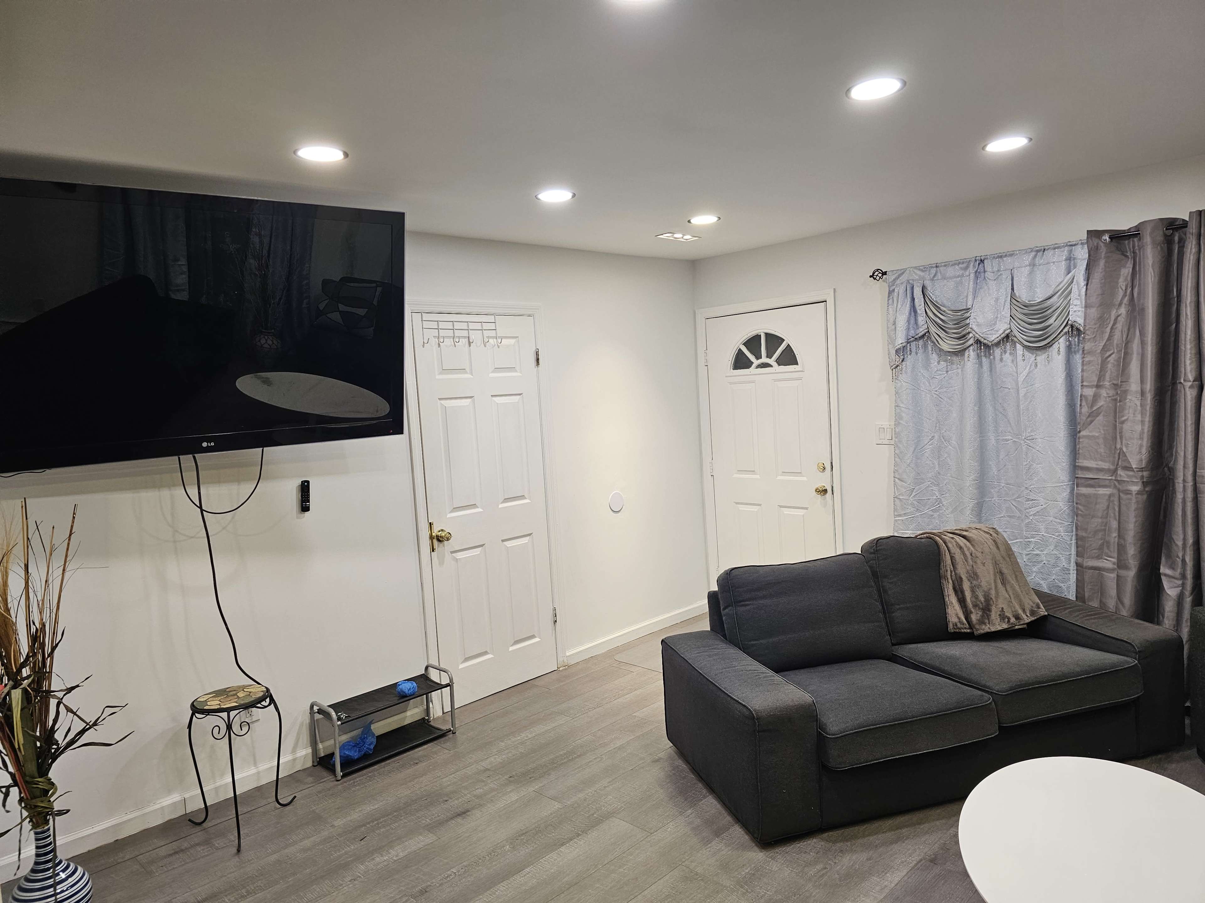 A living room features a gray sofa, a mounted television, a white coffee table, and a doorway with a decorative curtain.