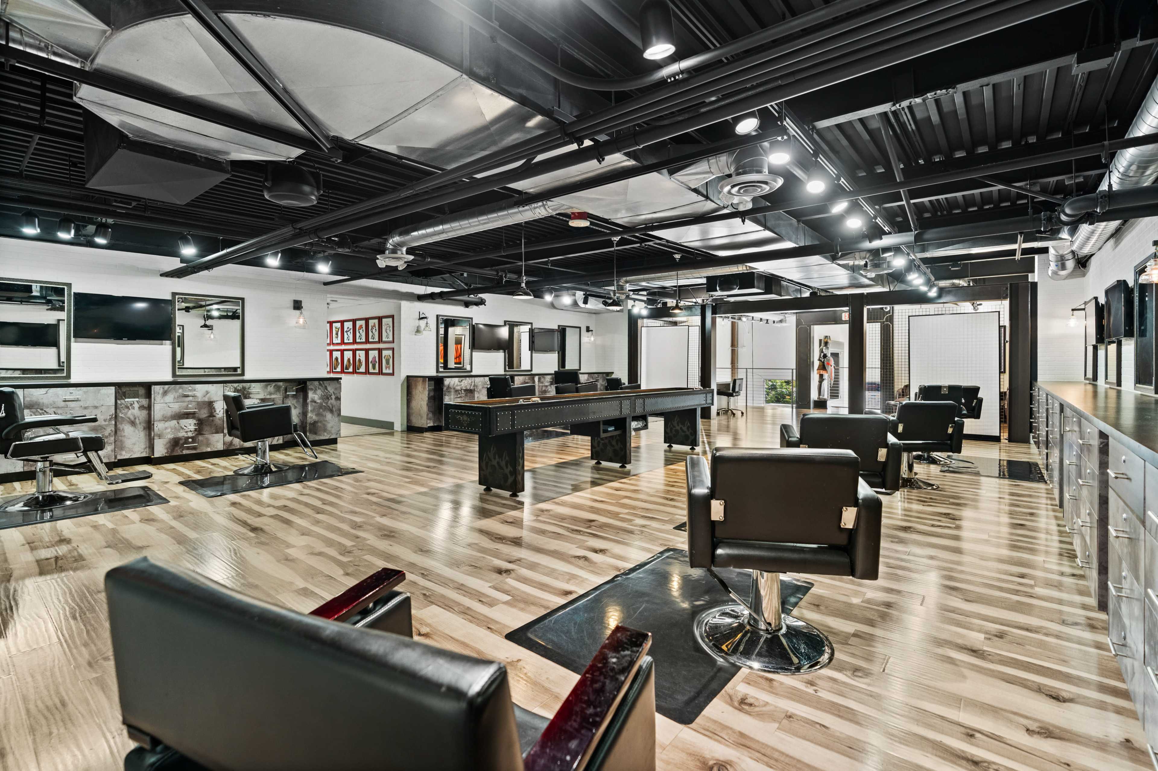 The image shows a modern hair salon with several black styling chairs arranged around a central work area and large mirrors on the walls.