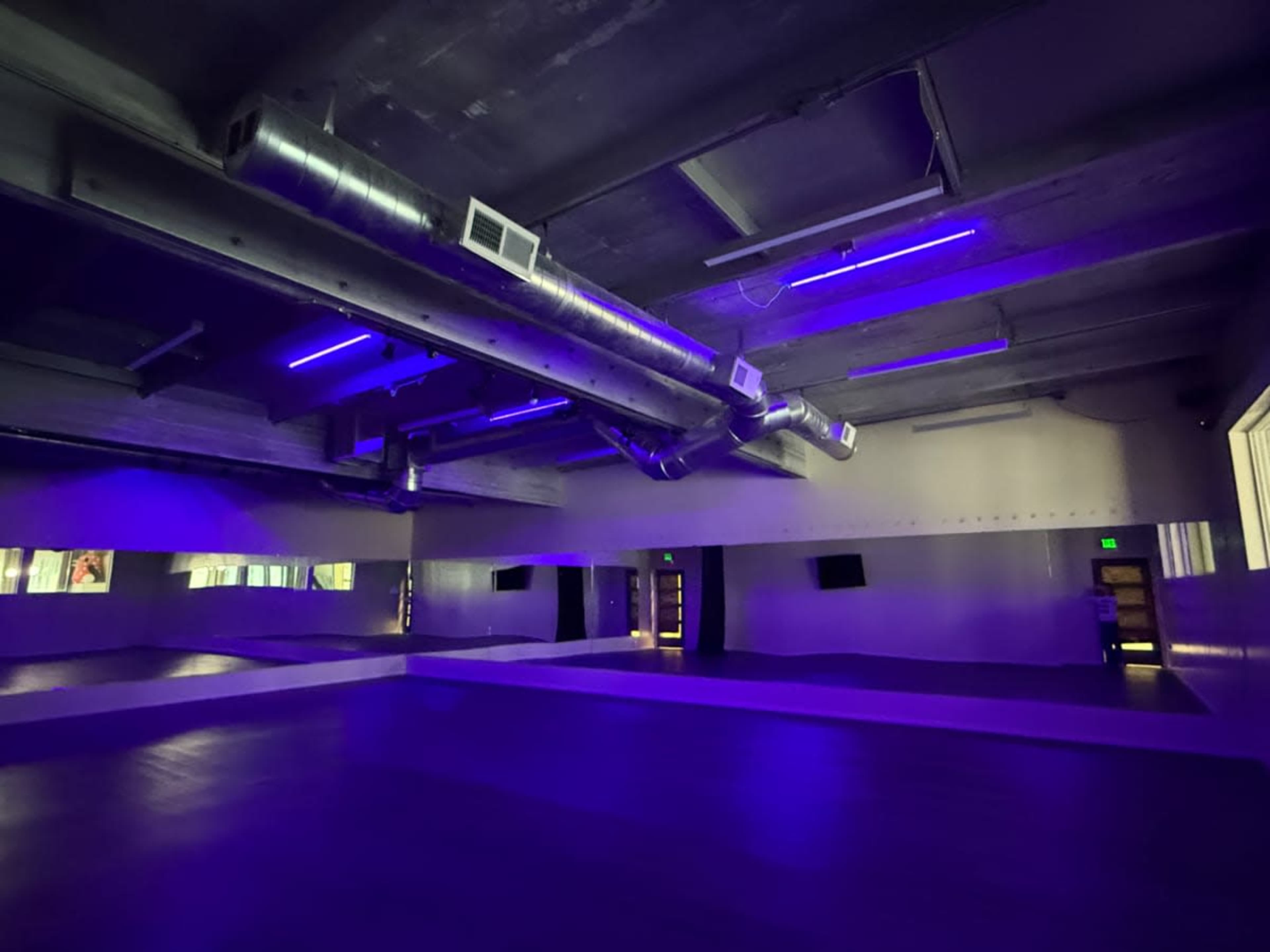 The image shows an empty dance studio with purple LED lighting and mirrors along the walls.