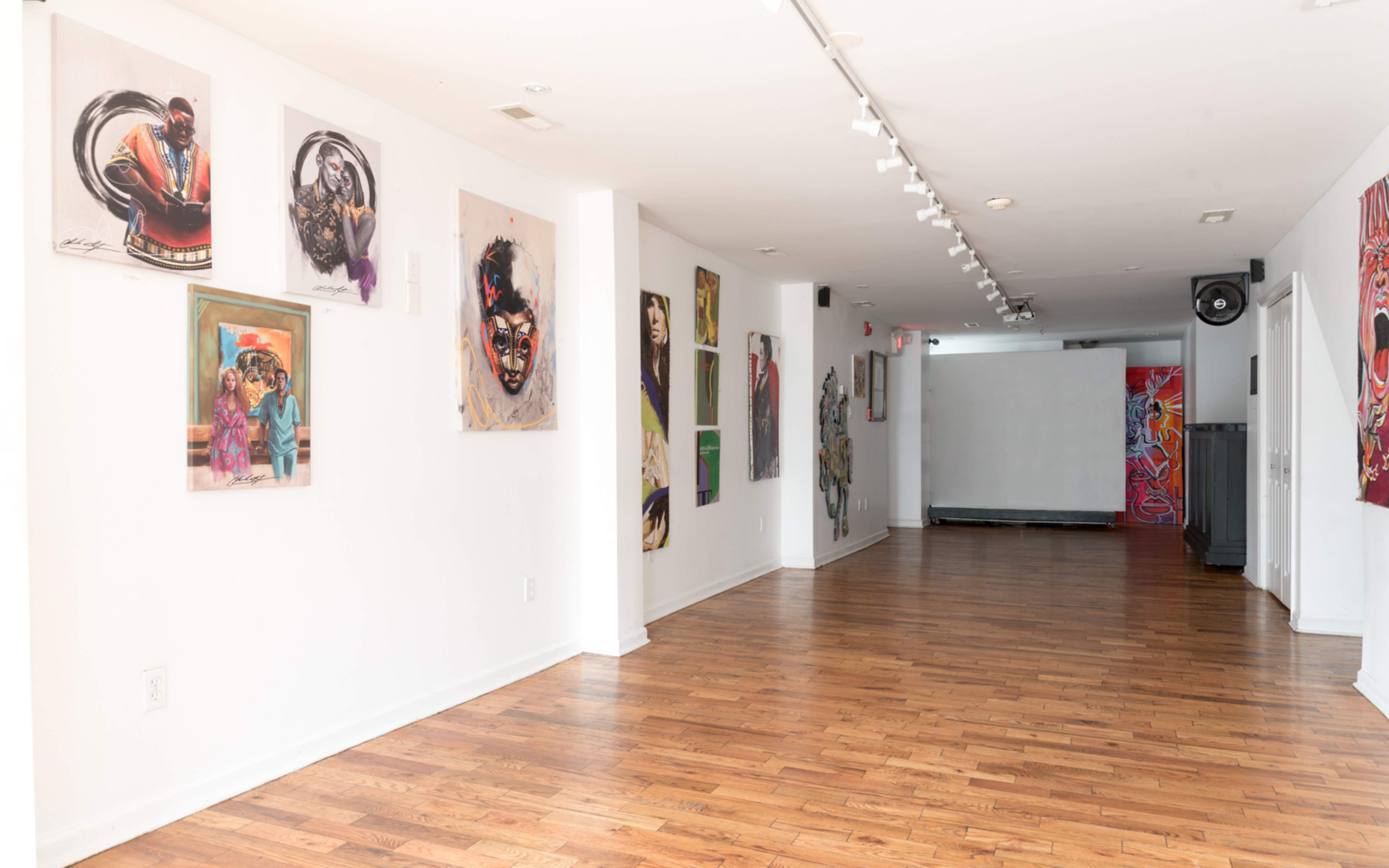 A modern art gallery featuring various colorful artworks displayed on the white walls, with polished wooden floors and bright lighting.