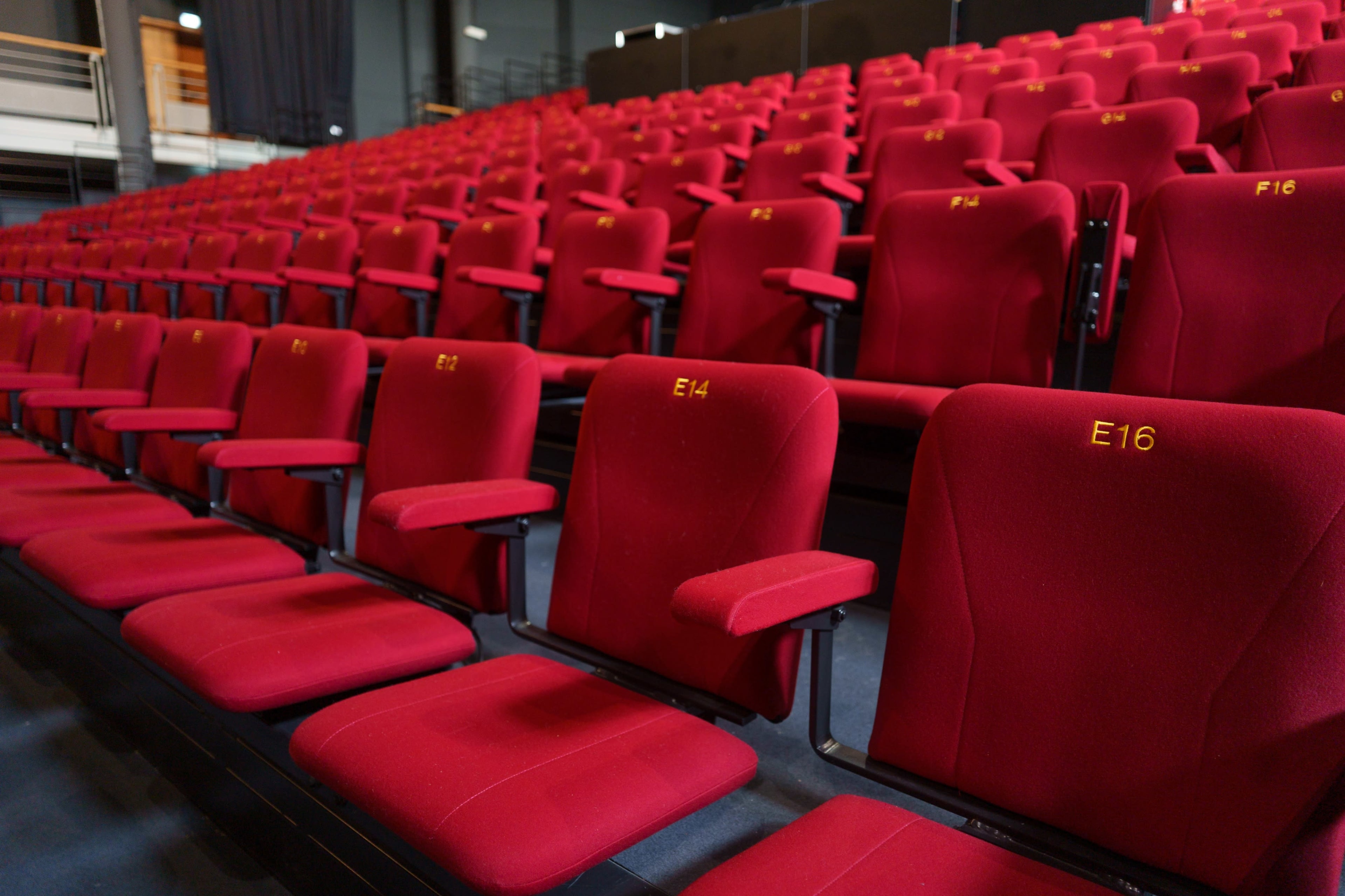 A section of empty red theater seats arranged in rows, with some seats labeled with numbers.