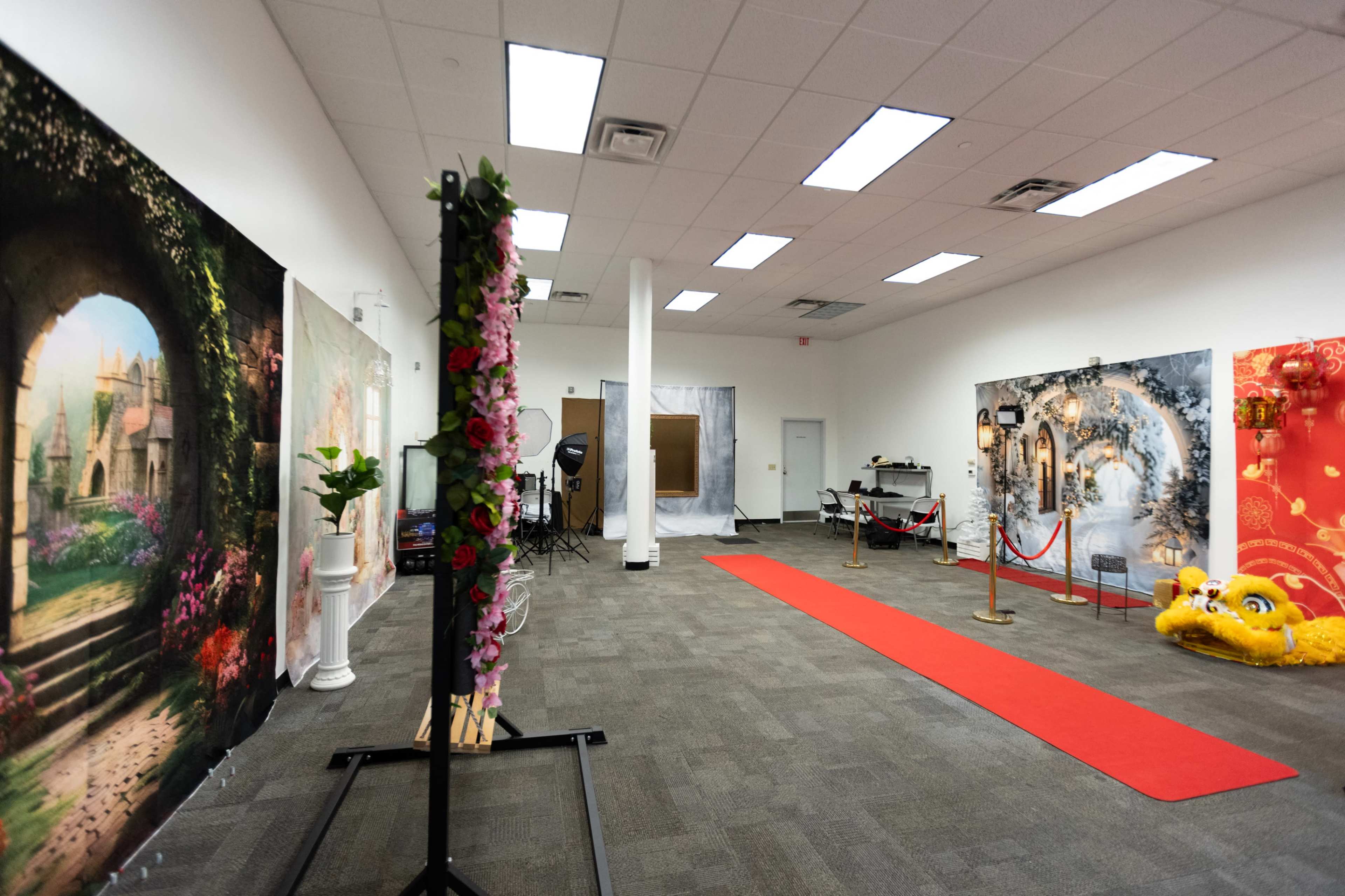 The image shows an event space featuring a red carpet, floral decorations, and large backdrops with scenic designs.