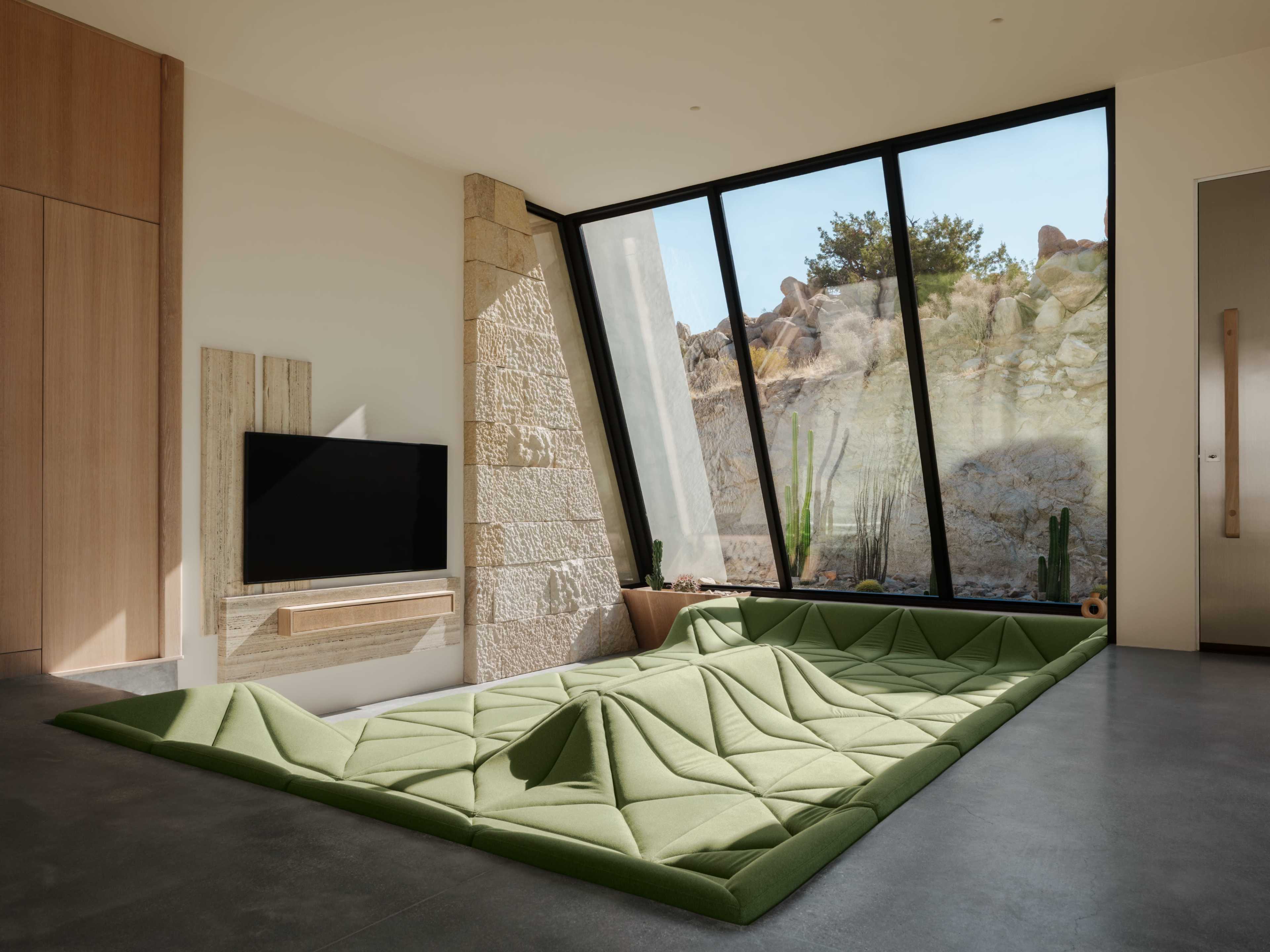 A modern living room features a green, sculptural seating area below a large angled window that offers a view of rocky outdoor scenery.