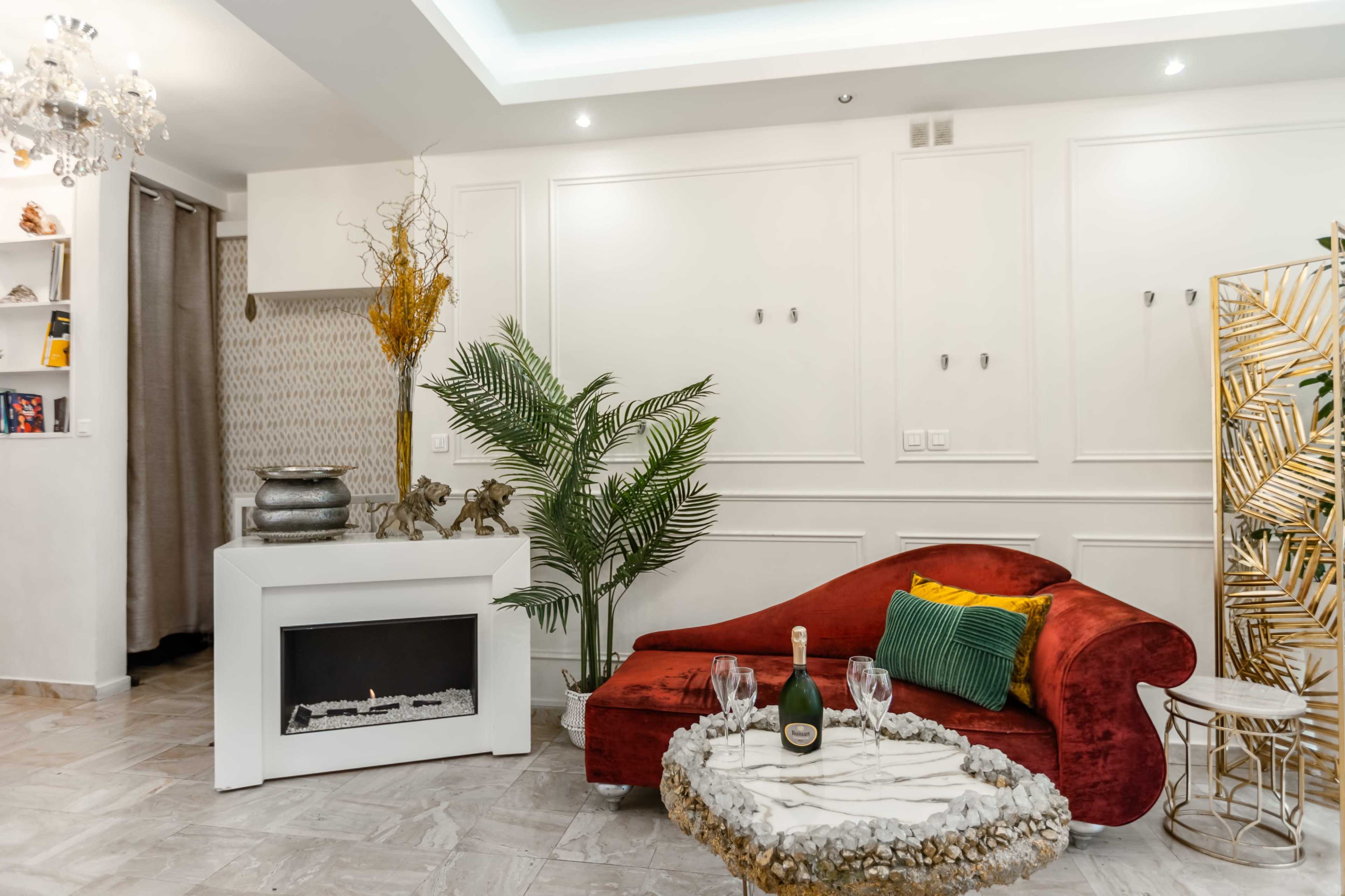 The image shows a stylish living room featuring a red curved sofa, a coffee table with decorative stones, a potted plant, and a modern electric fireplace.