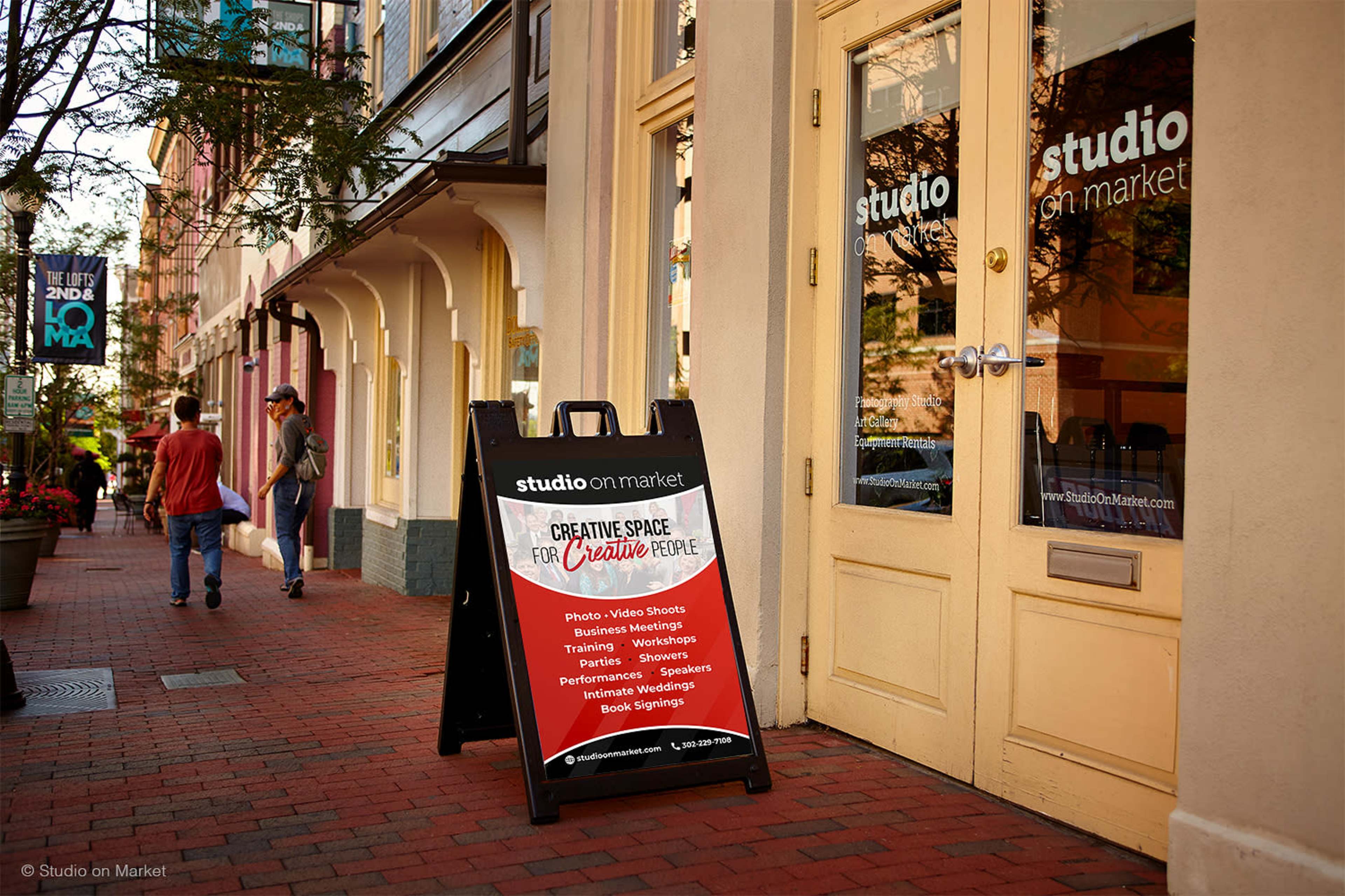 A sandwich board outside a creative space lists various services for artists and performers in a pedestrian area.
