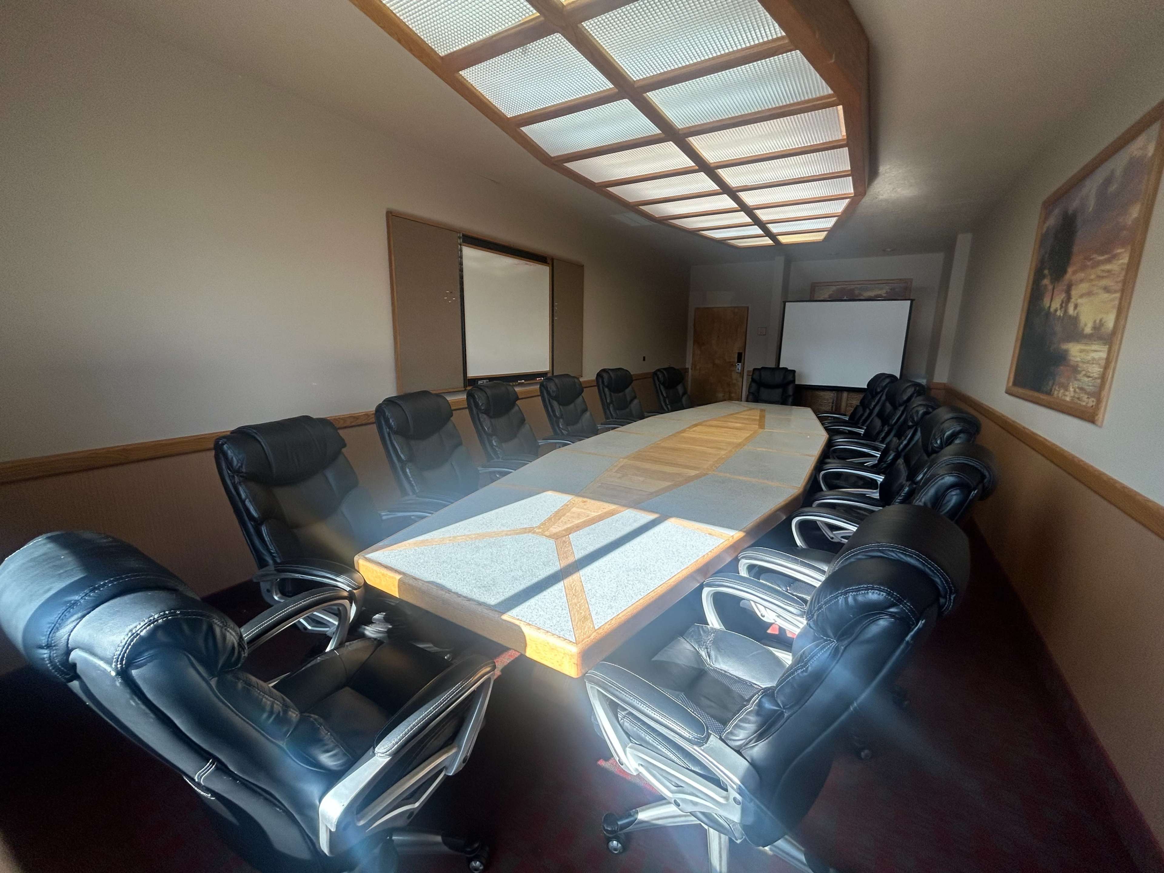 The image shows a large, empty conference room featuring a long, oval table surrounded by black chairs and equipped with overhead lighting.