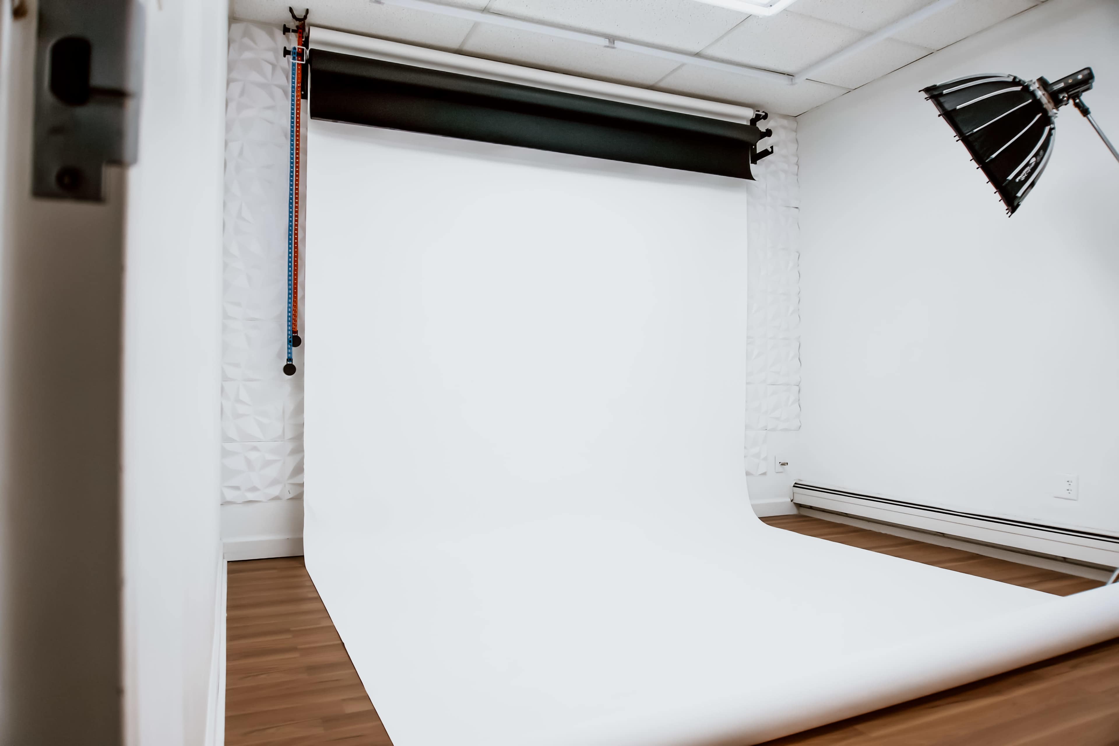The image shows a photography studio with a white backdrop and wooden flooring.